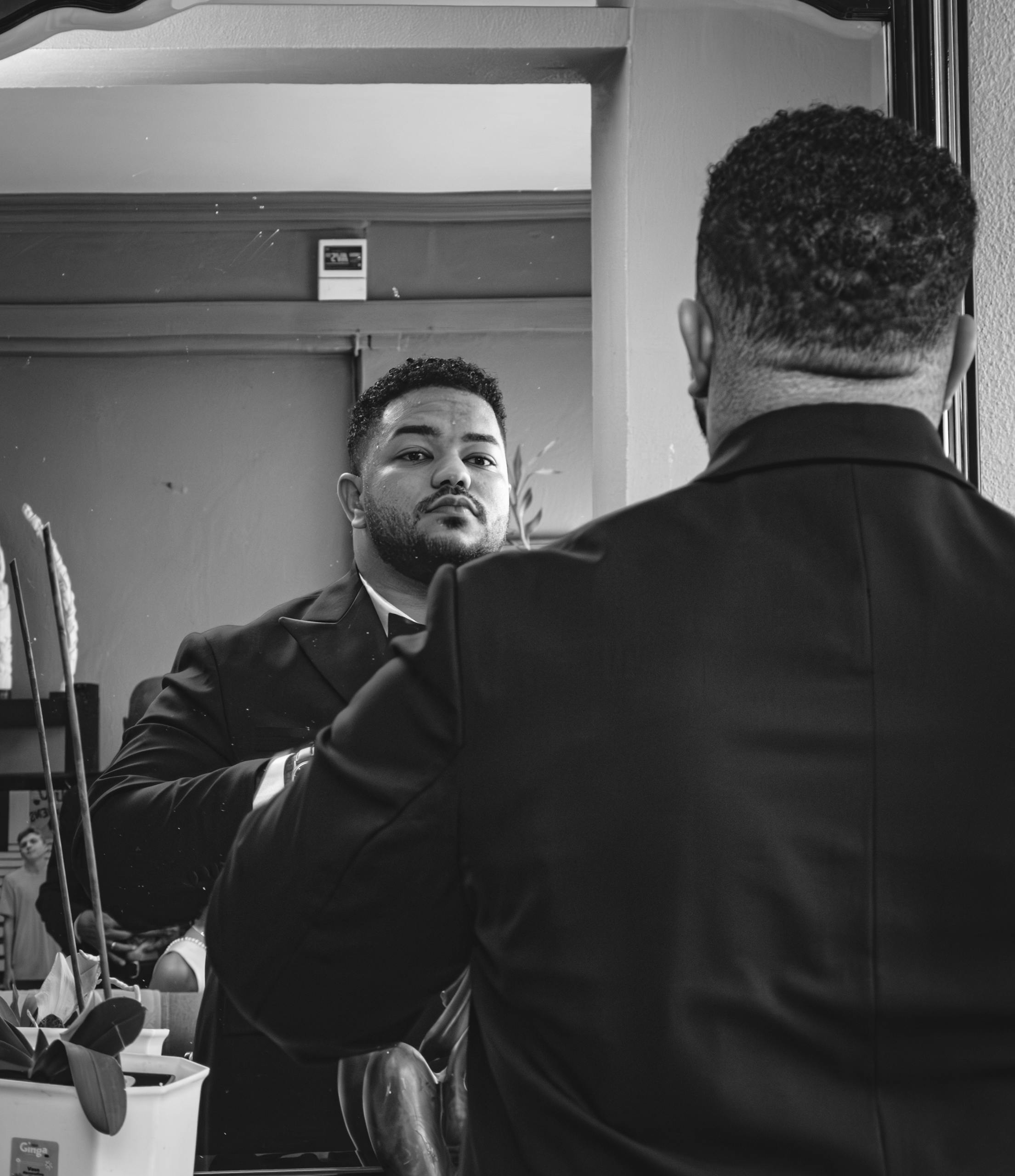 A man in a suit checks his appearance in a mirror, adding a contemplative and stylish vibe to the scene.