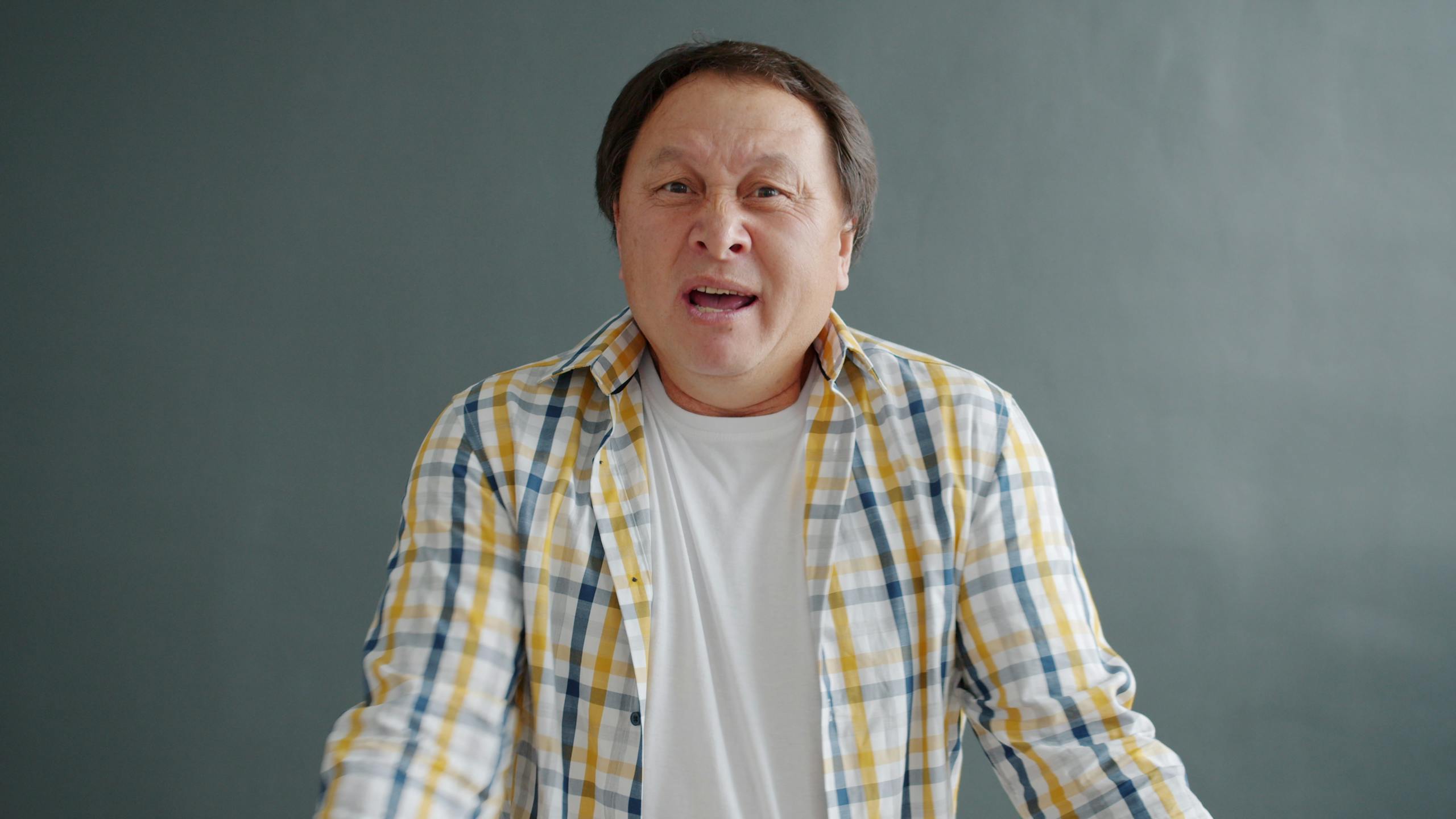 A man in plaid shirt expressing surprise against a gray background.