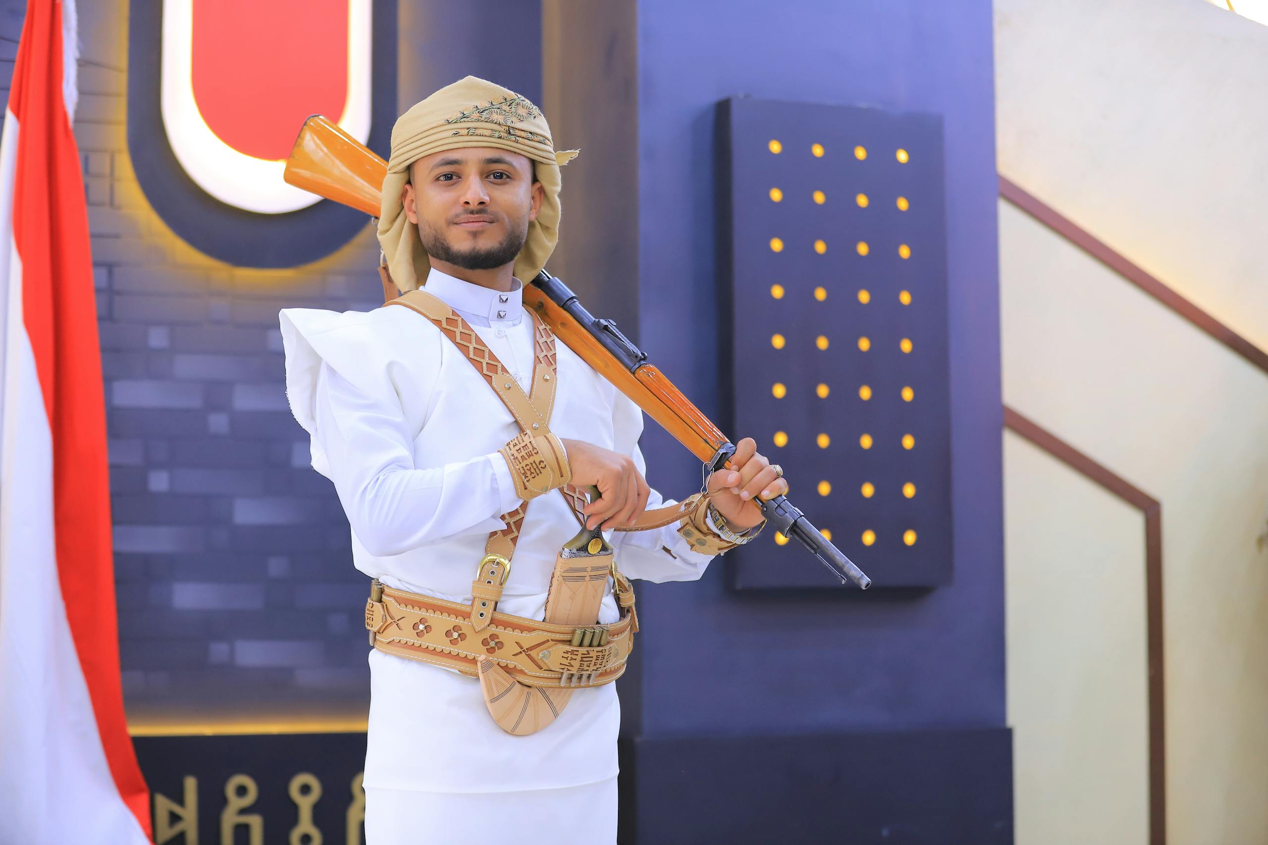 A man in traditional Yemeni dress poses with a rifle indoors in Sana'a, Yemen.