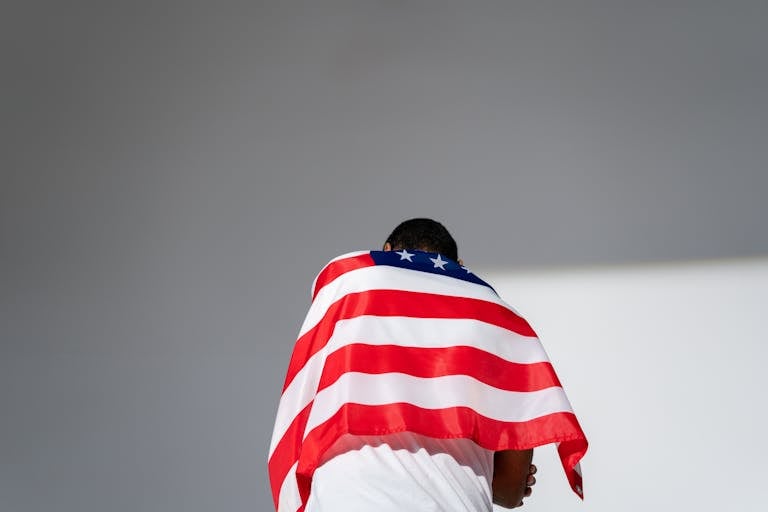 A man stands wrapped in the American flag, symbolizing national pride and patriotism.