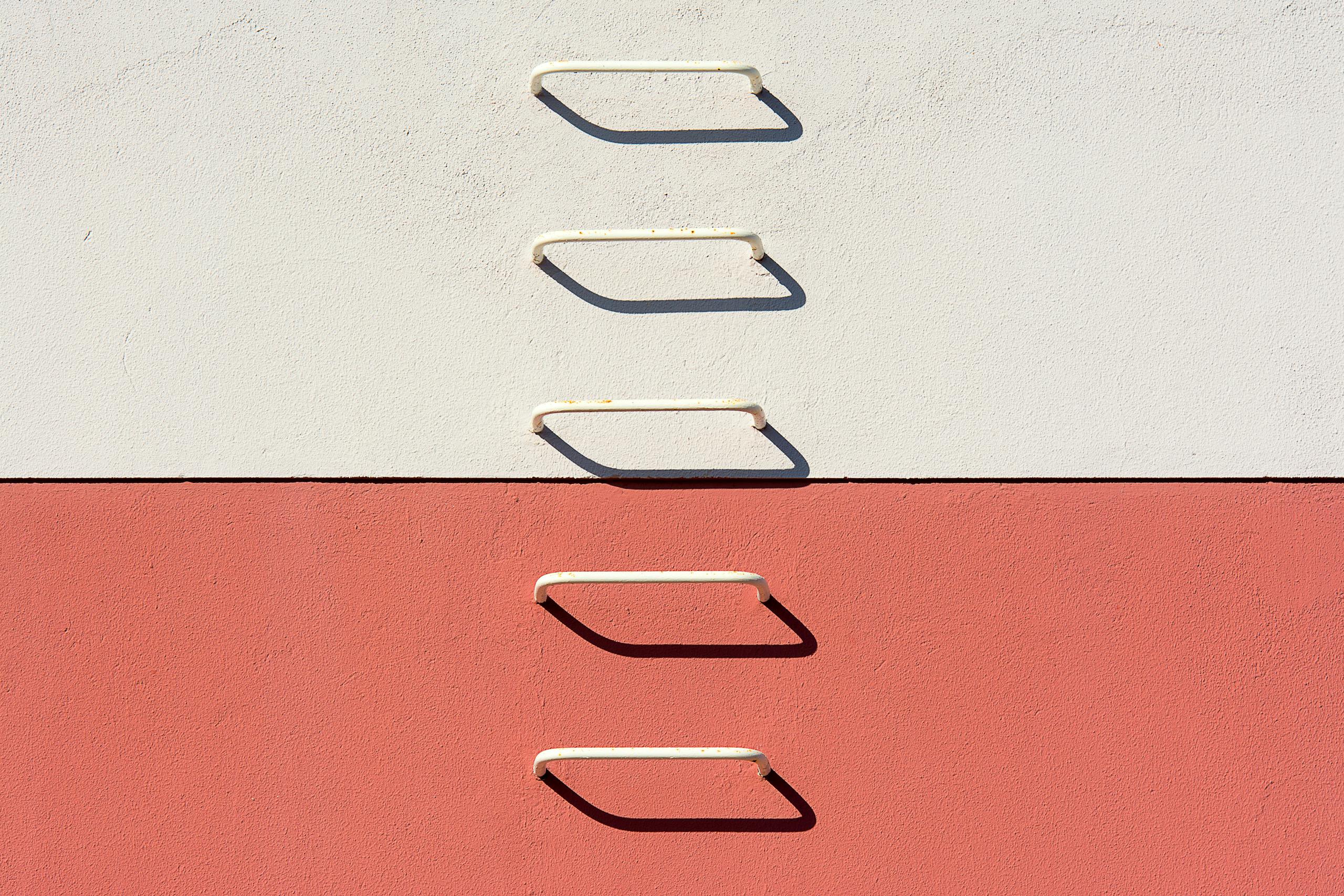 A minimalist view of a metal ladder casting shadows on a divided white and red wall.