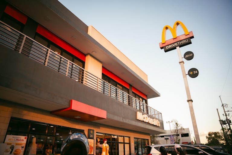 A modern McDonald's fast food restaurant with distinctive branding and drive-thru facilities under a clear blue sky.