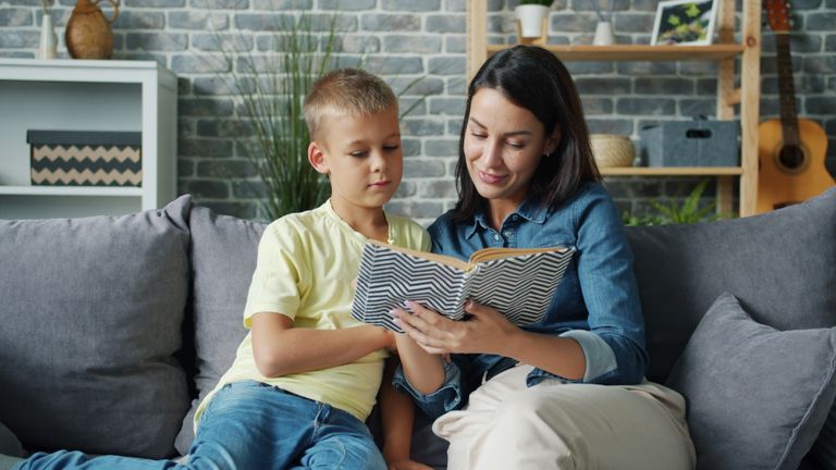 A mother and son enjoy reading a book together on a cozy couch in a modern living room.