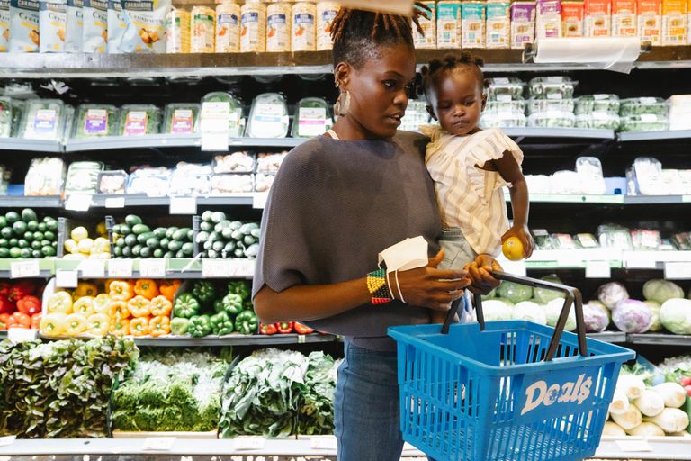 A mother carries her child while shopping in the supermarket's fresh produce section.