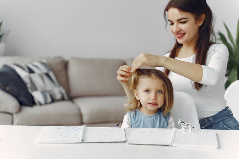 A mother styles her daughter's hair in a cozy living room setting, capturing a moment of love and togetherness.