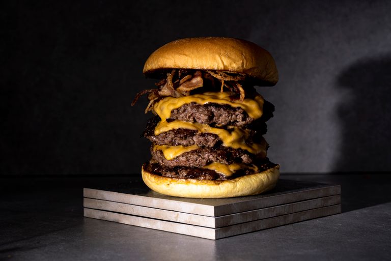 A mouthwatering triple cheeseburger with melted cheese, crispy bacon on a stone slab.