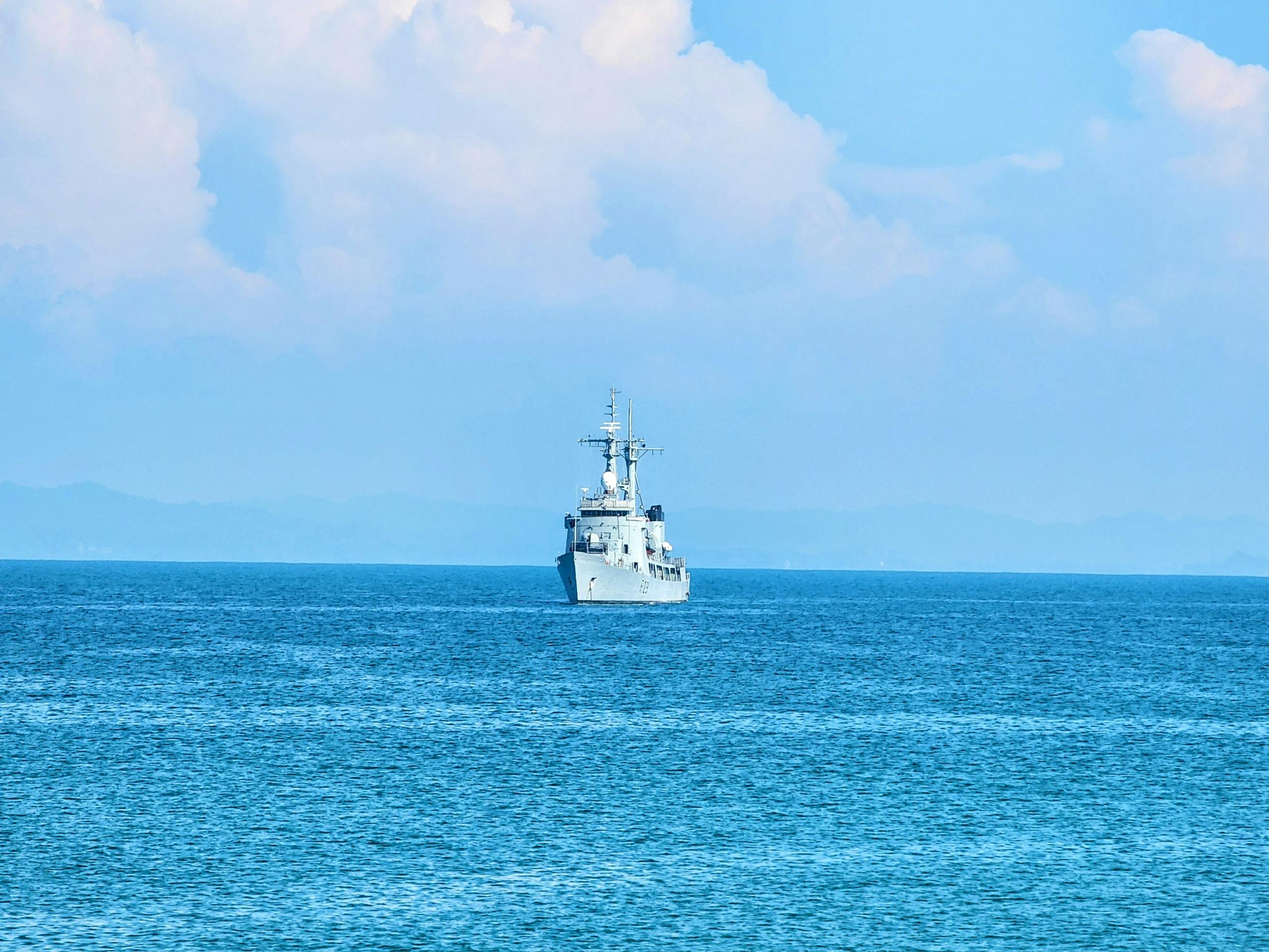 A naval vessel sailing across a calm blue ocean under a clear sky.