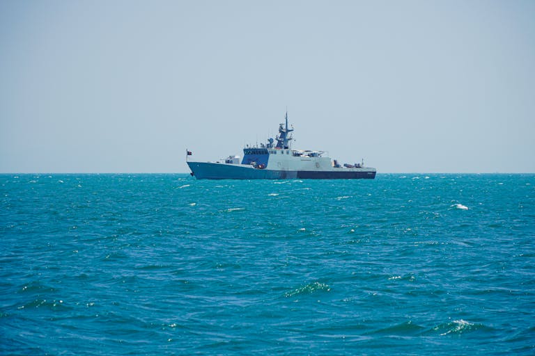 A navy patrol ship sailing on clear tropical waters under a bright sky.