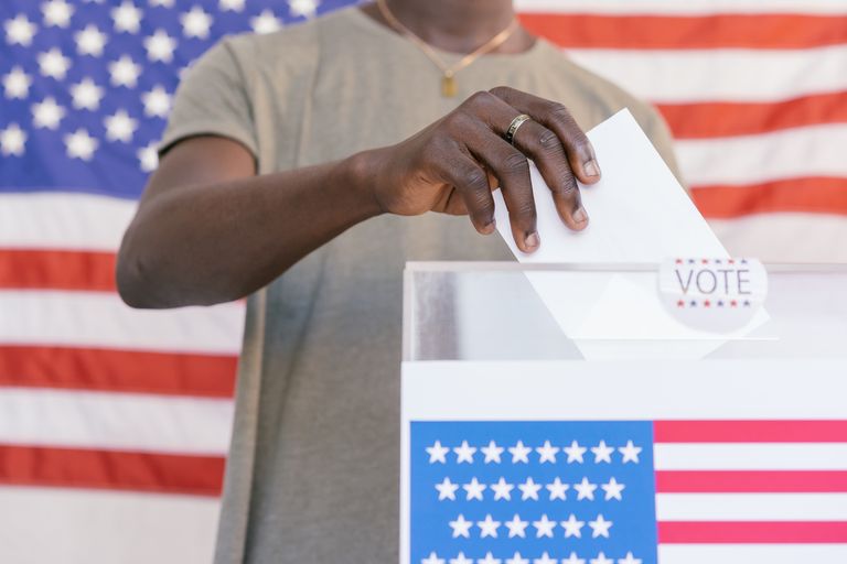 A person casting their vote at a polling station with a US flag in the background.