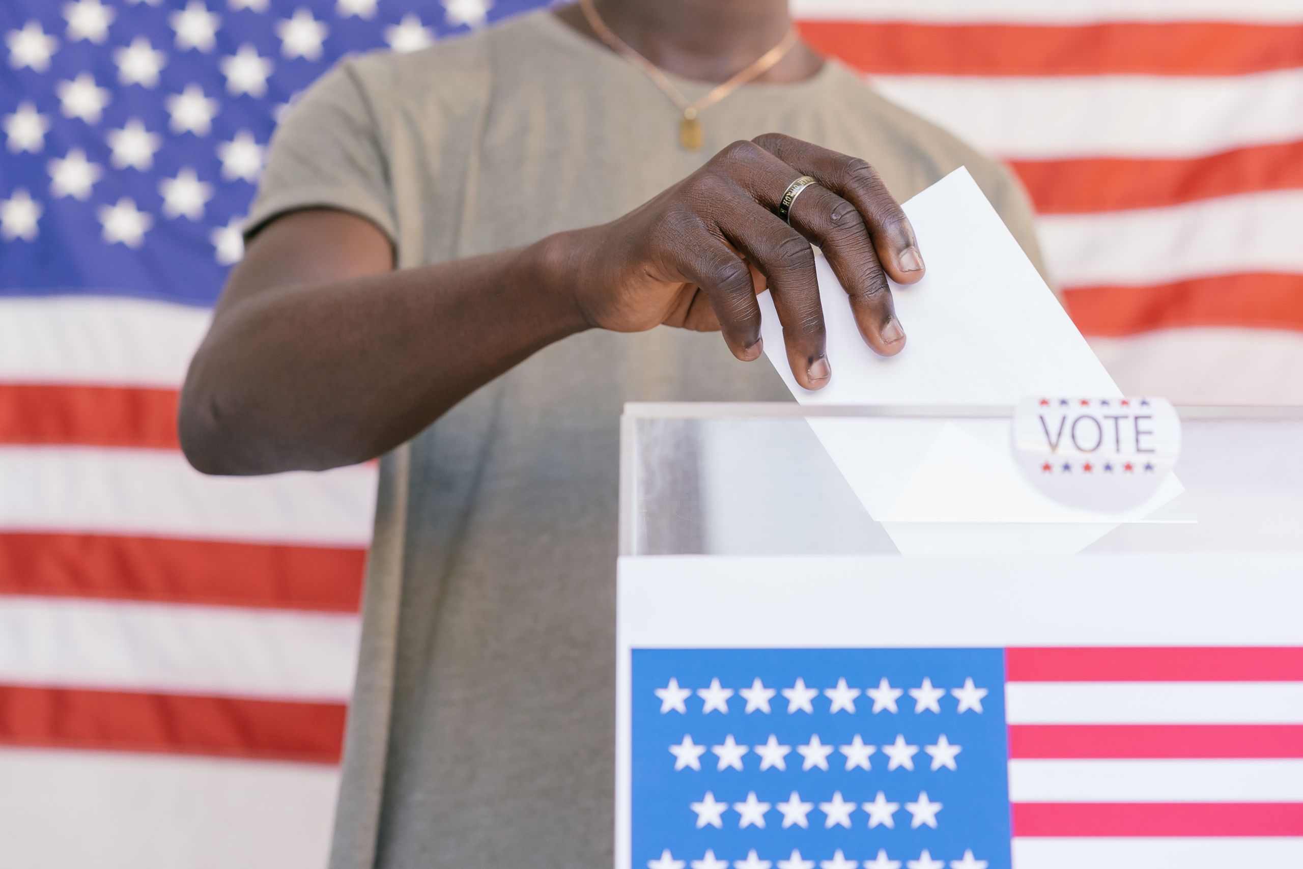 A person casting their vote at a polling station with a US flag in the background.