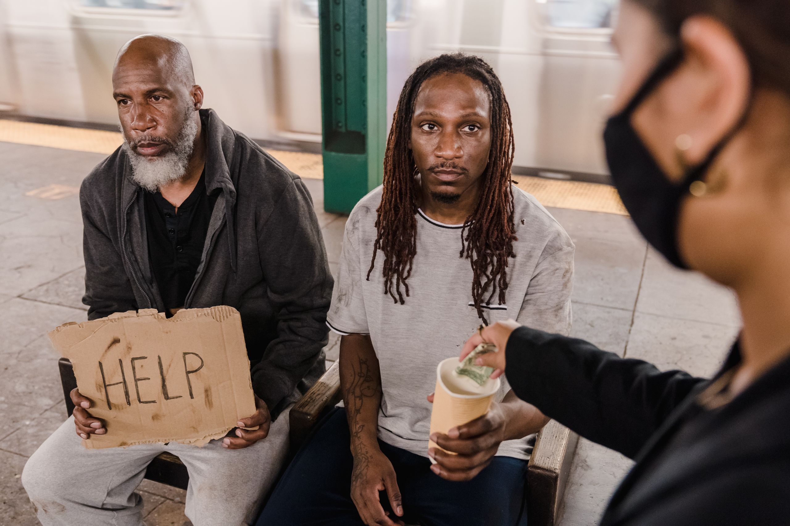 A person gives assistance to two homeless men in a subway station.