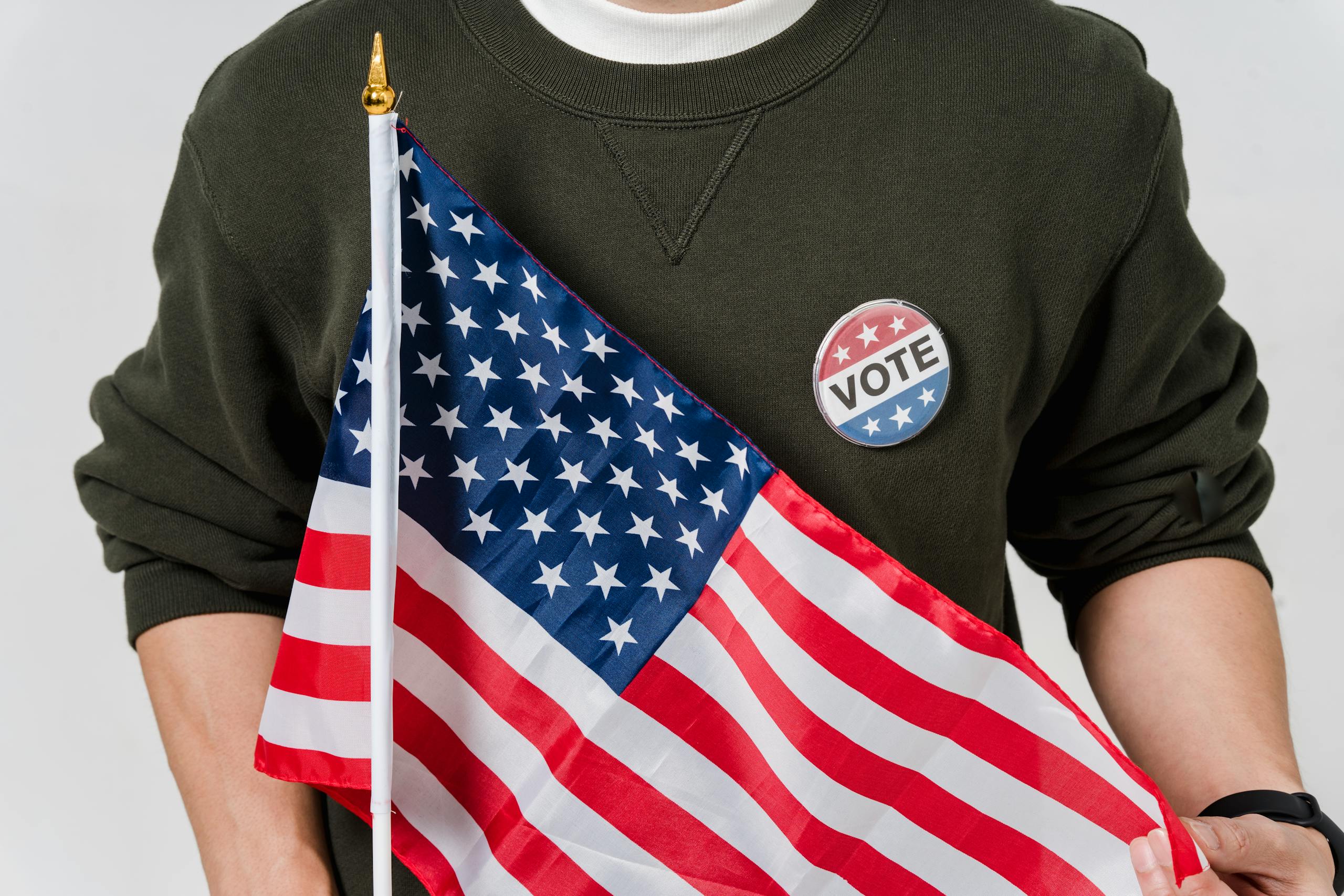 A person holding an American flag with a vote badge, symbolizing patriotism and democracy.