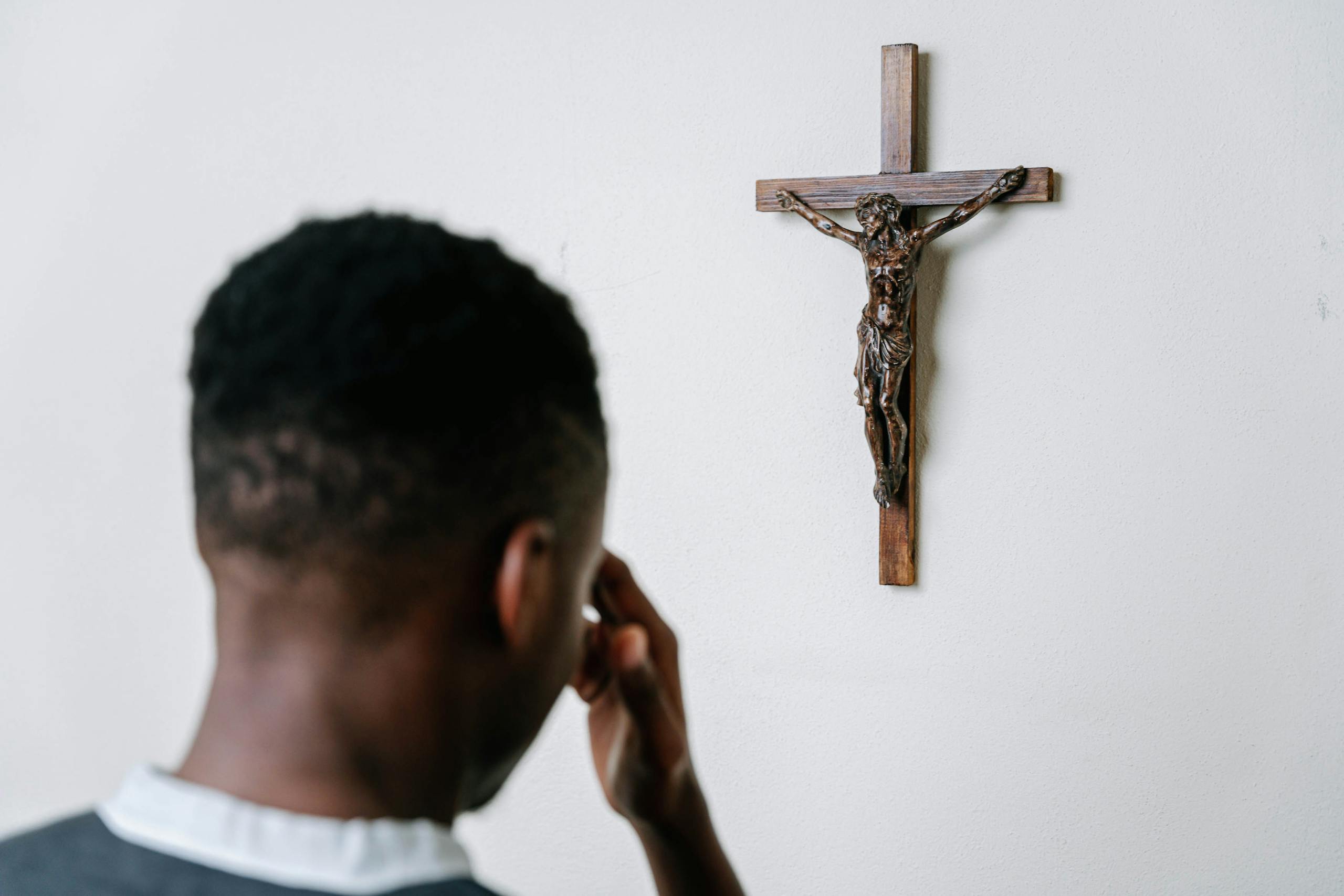 A person praying before a wooden crucifix on a plain wall, symbolizing faith and devotion.