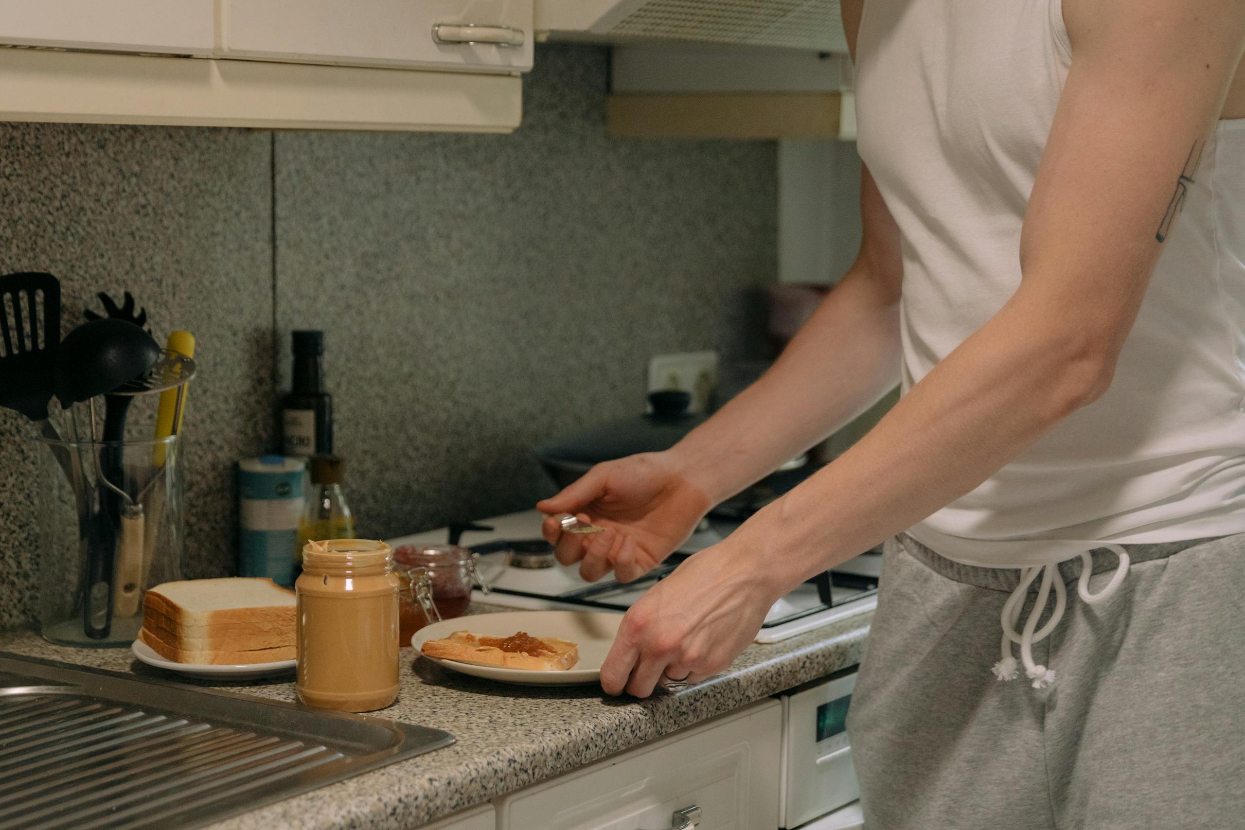 A person prepares a classic peanut butter and jelly sandwich on a kitchen counter.