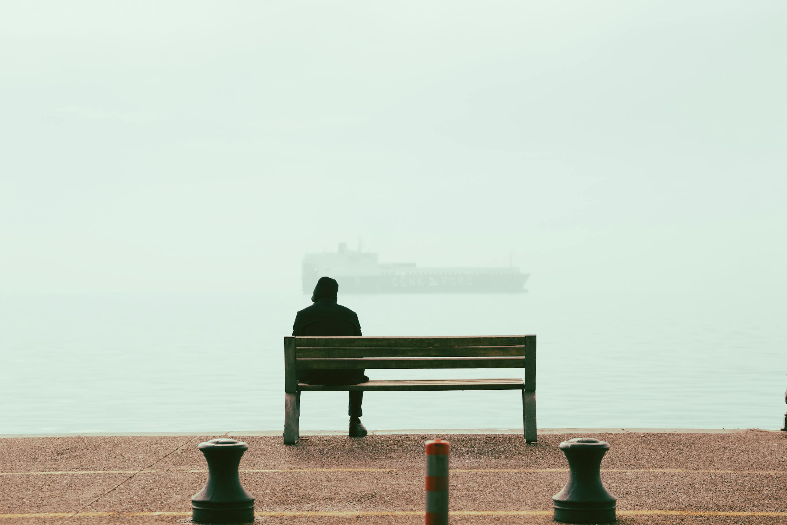 A person sits alone on a bench facing the sea in Thessaloniki, Greece, exuding a sense of solitude.