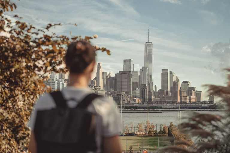 A person standing outdoors, looking at the New York City skyline on a sunny day.
