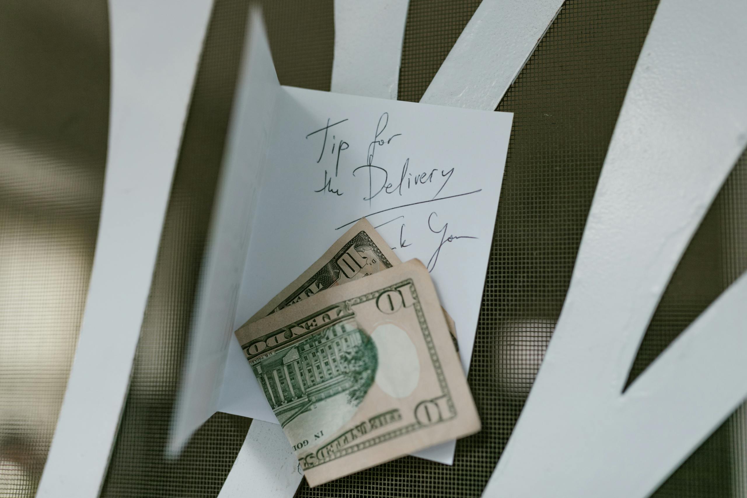 A photo of US dollar bills placed with a handwritten tip note for delivery service.