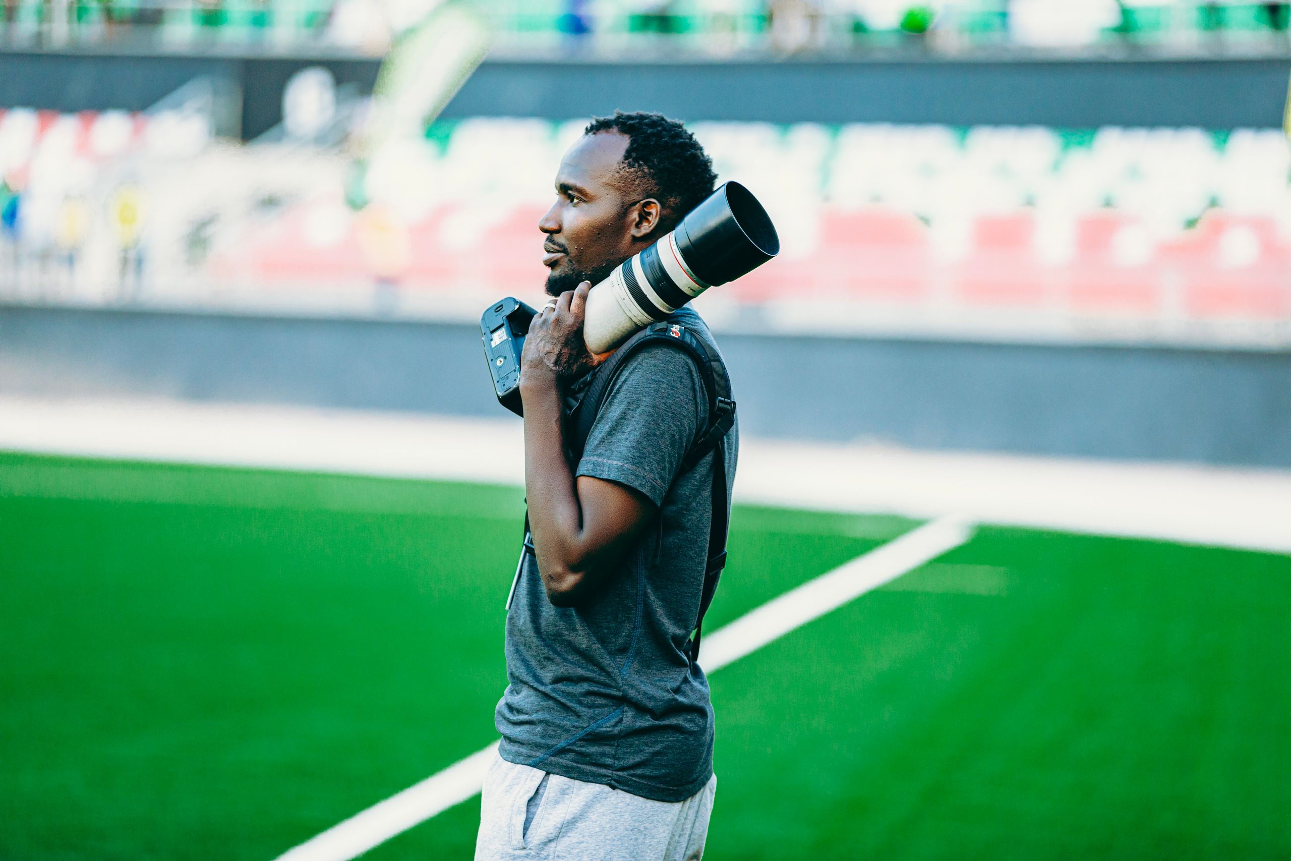 A photographer with a long lens camera stands on a sports field, capturing the action.