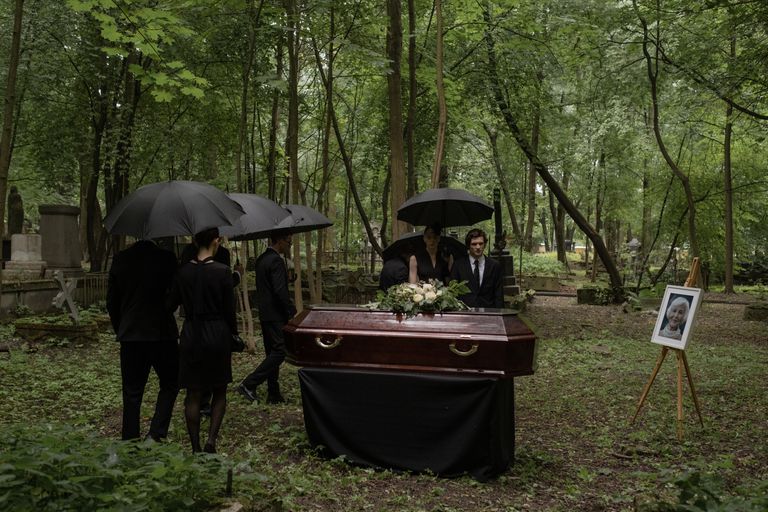 A poignant funeral scene in a wooded cemetery with mourners, a coffin, and somber atmosphere.