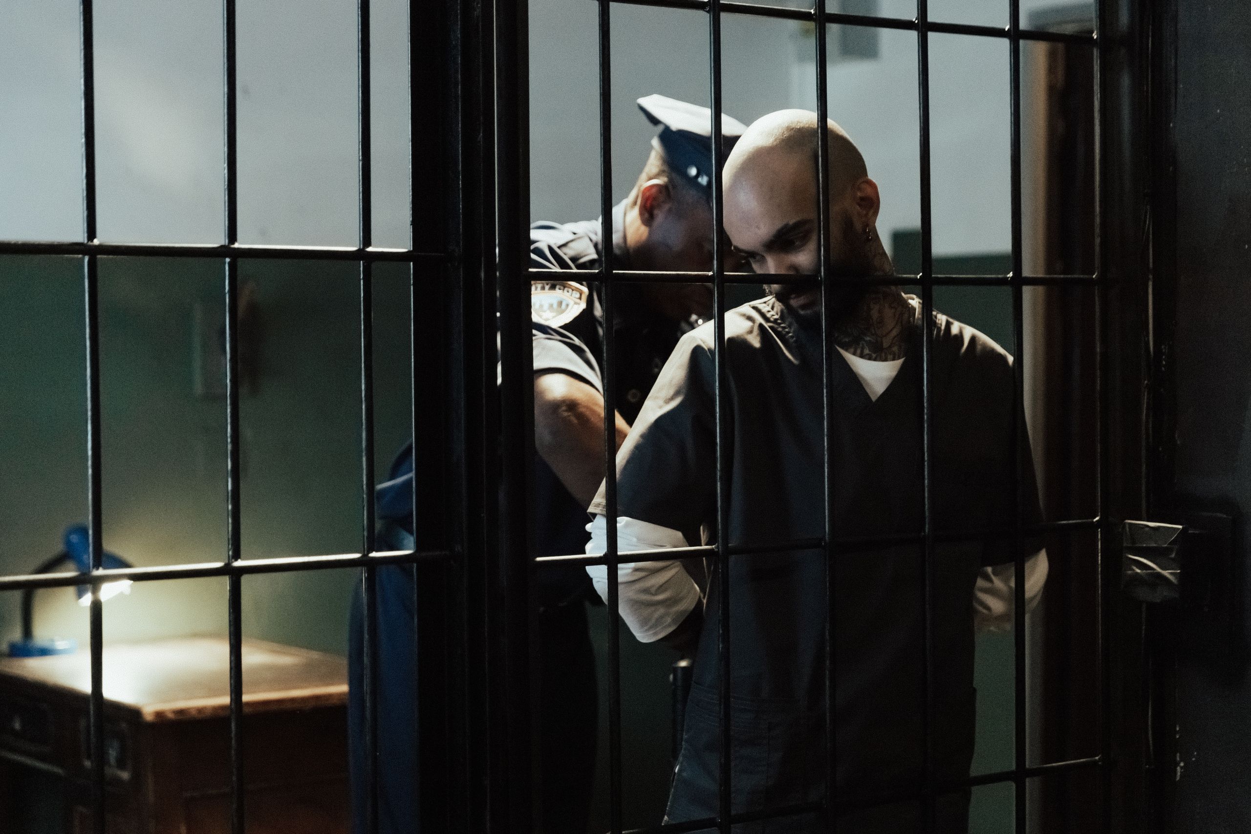 A police officer handcuffing a male prisoner inside a cell with bars.