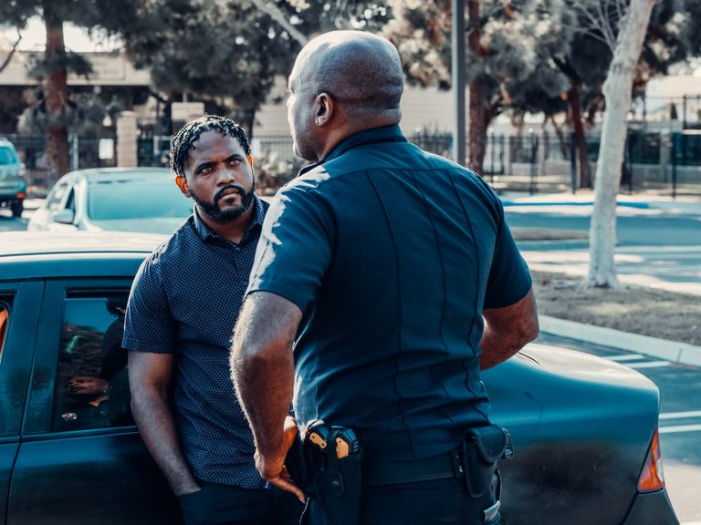 A police officer talking to a man beside a car on a sunny street.