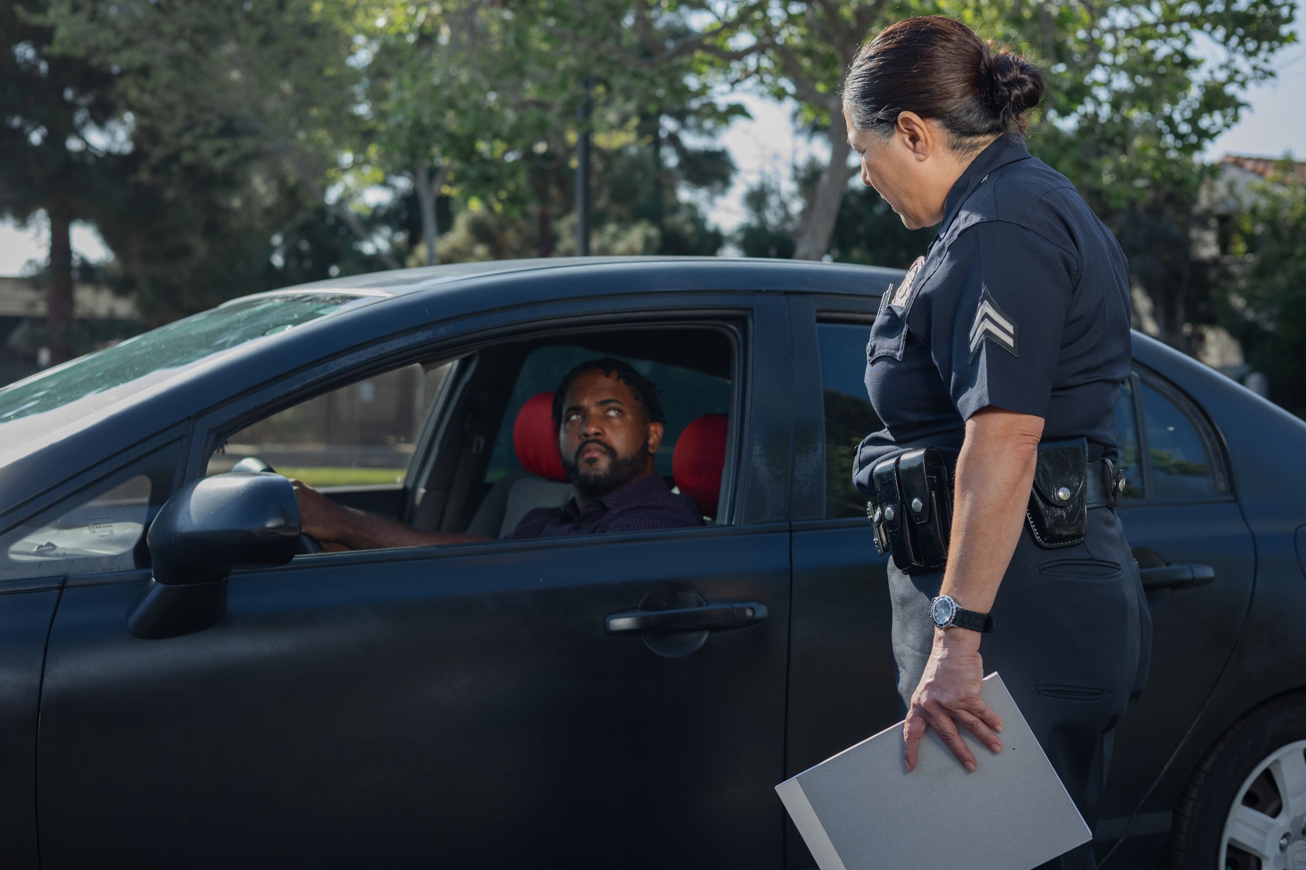 A policewoman discusses a traffic violation with a driver on a sunny day.