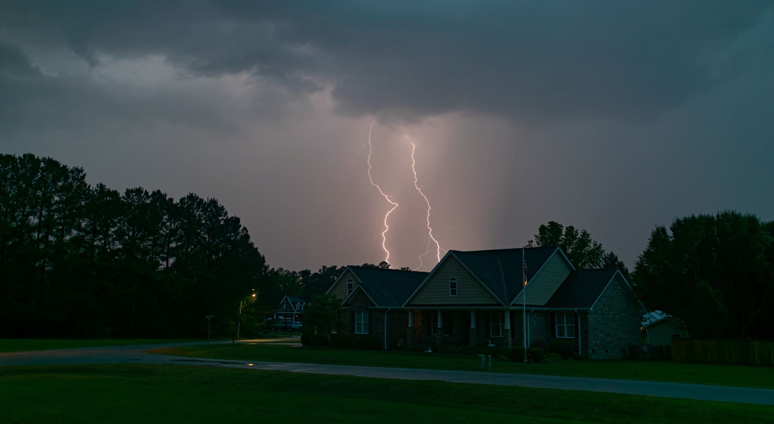 A powerful lightning bolt illuminates a suburban neighborhood under an overcast sky.