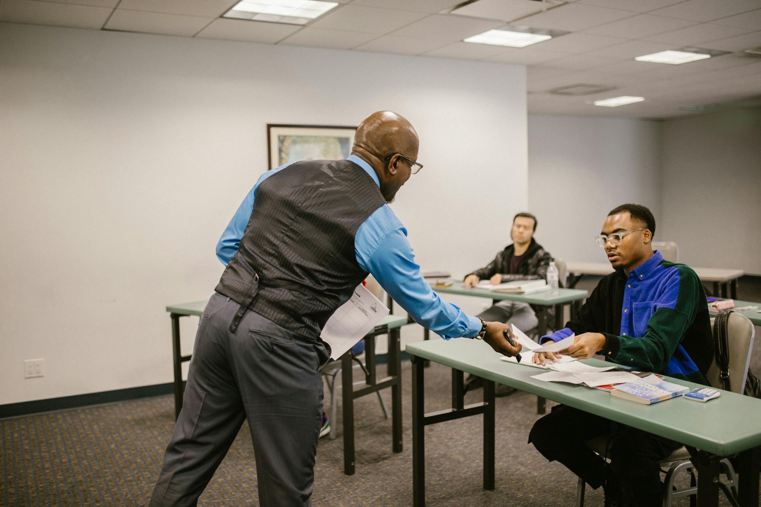 A professor hands out test papers to college students in a classroom, fostering an educational environment.