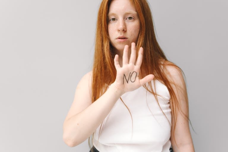 A red-haired woman expresses refusal with an open hand gesture, wearing a white tank top.