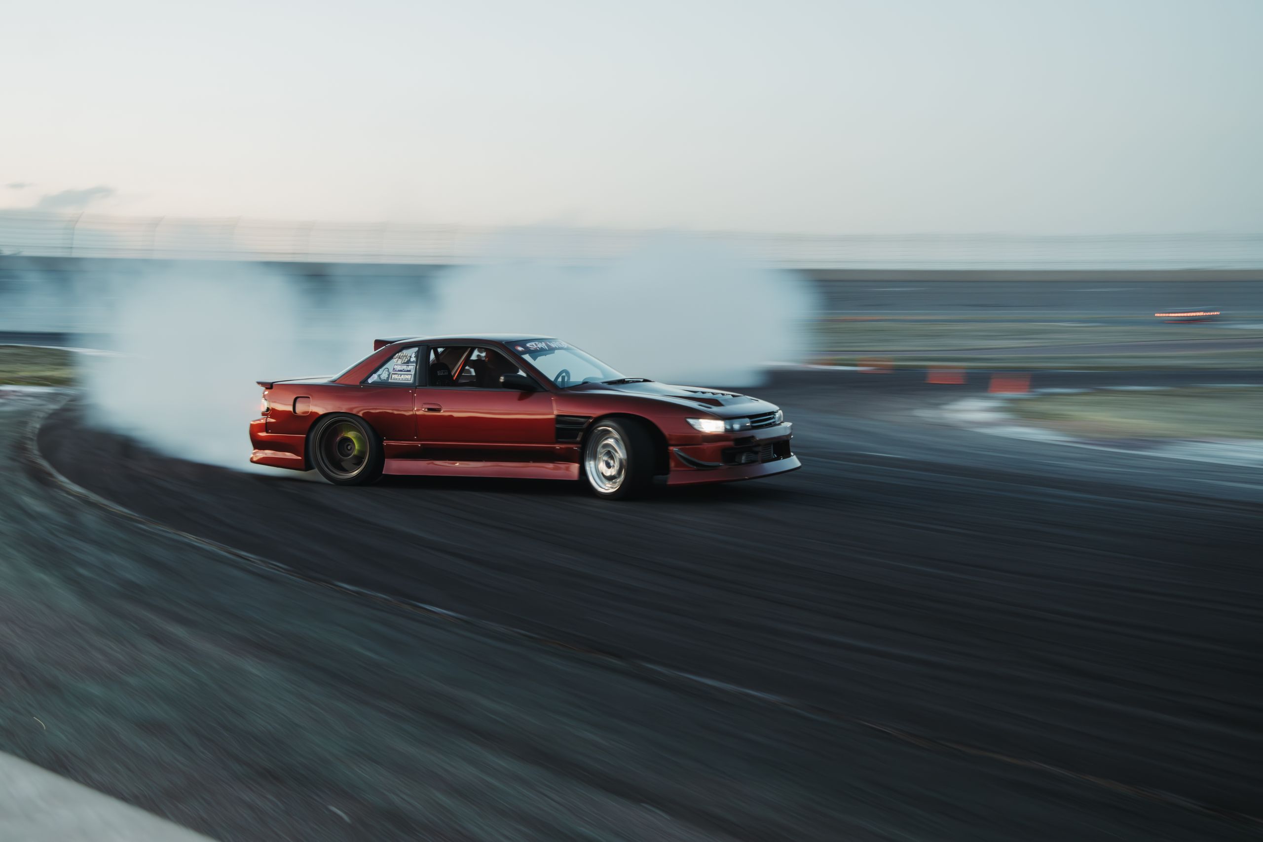A red Nissan racecar performs a dramatic drift on a racetrack in Colorado, capturing speed and precision.