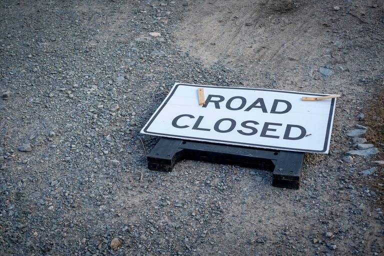 A road closed sign lies on a gravel pathway, indicating a blocked road ahead.