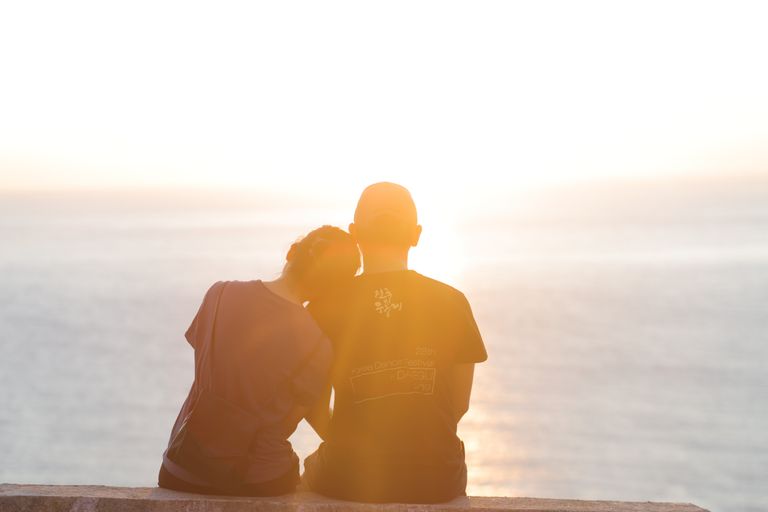 A romantic couple sits side by side, enjoying a serene sunset by the sea in Đà Nẵng, Vietnam.