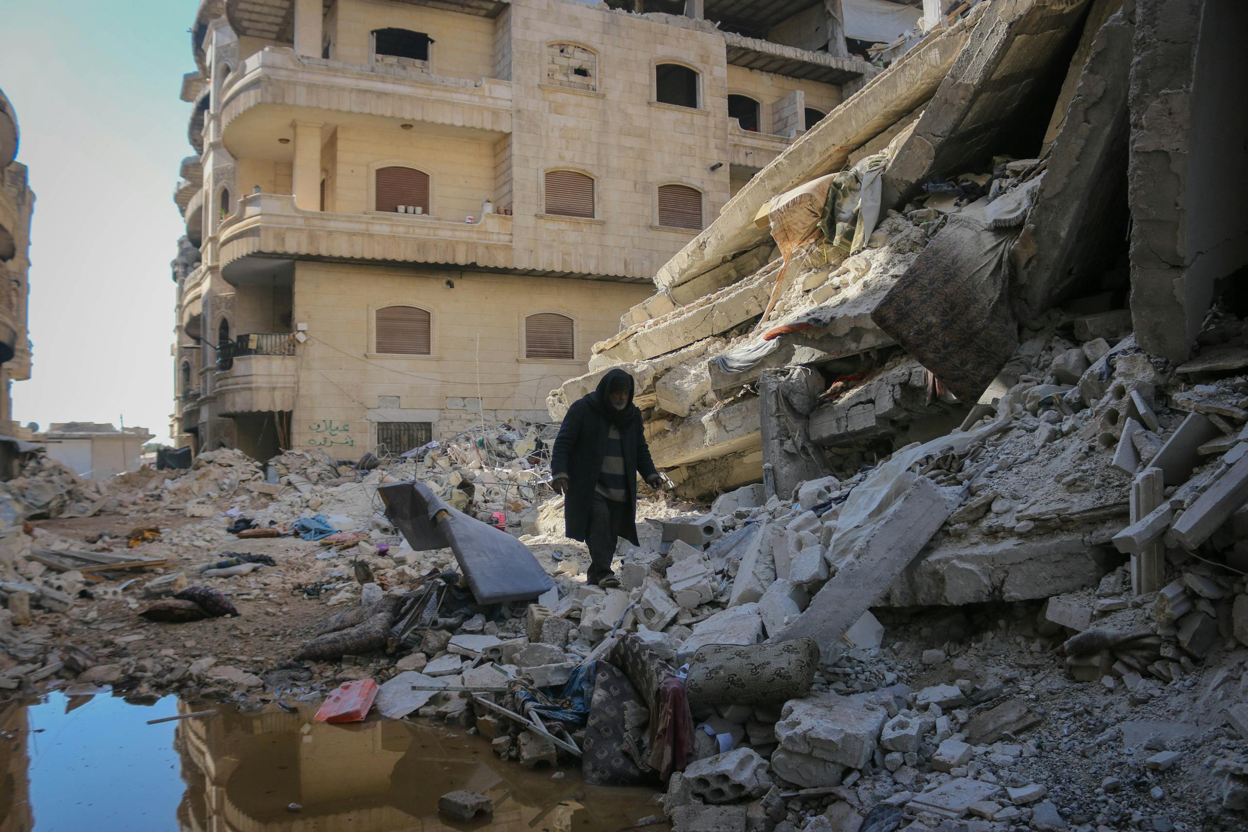 A scene of destruction in Idlib, Syria, shows the aftermath of urban conflict with debris and ruined buildings.