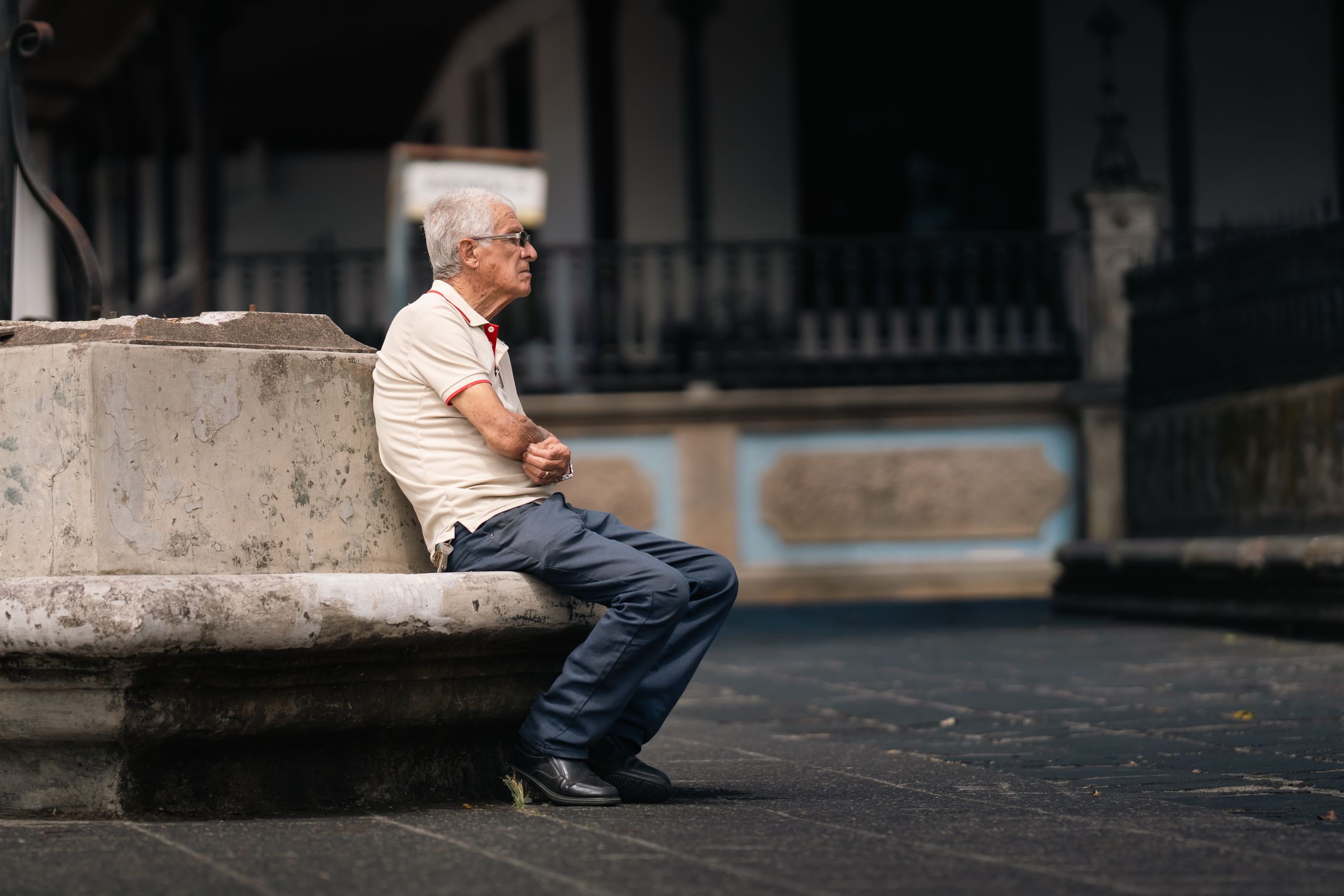 A senior adult sitting contemplatively on a stone bench in San Jos&eacute;, Costa Rica.