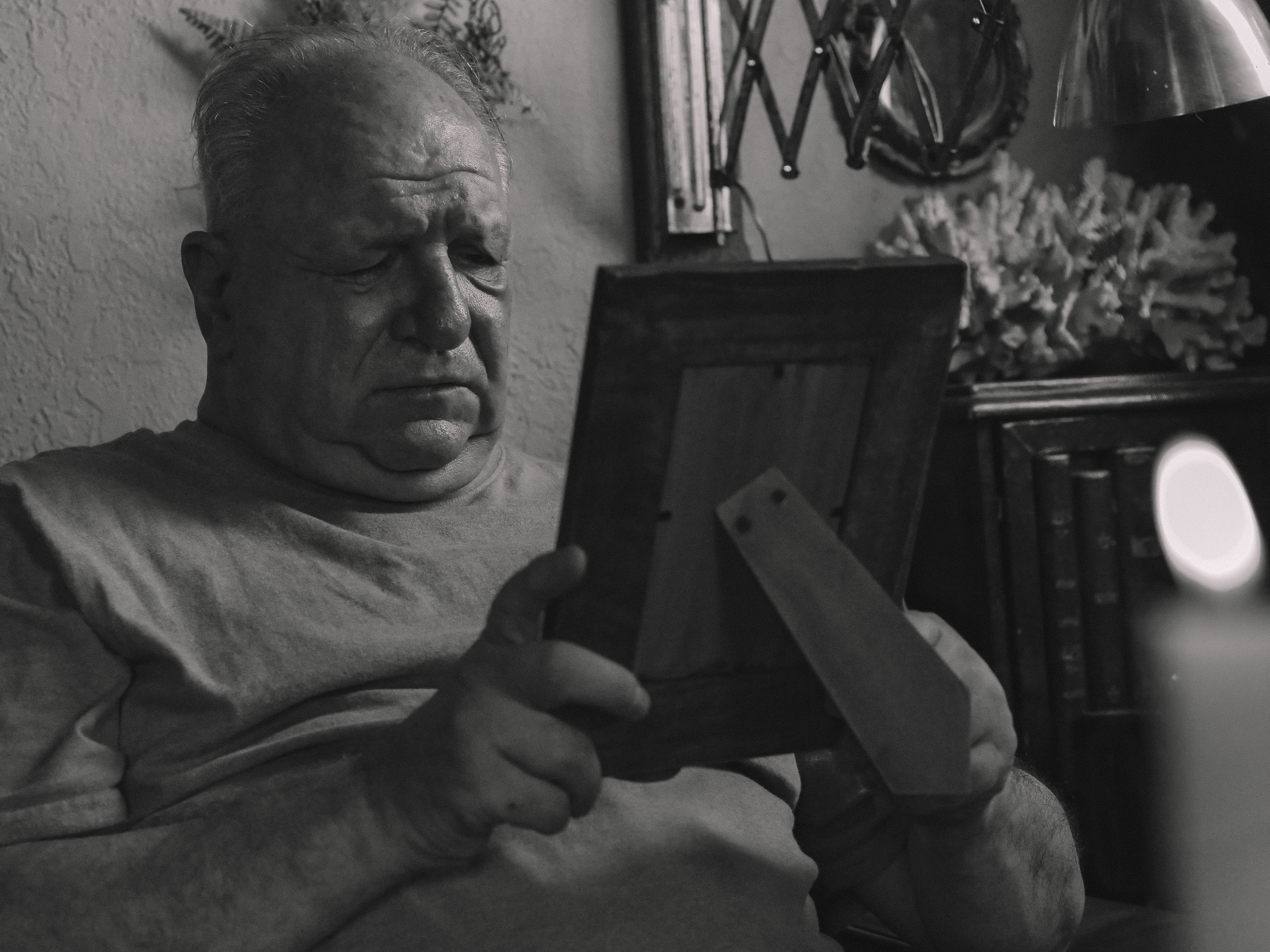 A senior man holding a picture frame looks reflective, conveying a sense of nostalgia.