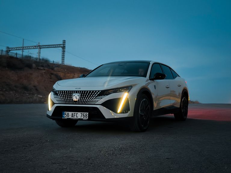 A sleek white car parked on a road during twilight, creating a moody and dramatic scene.