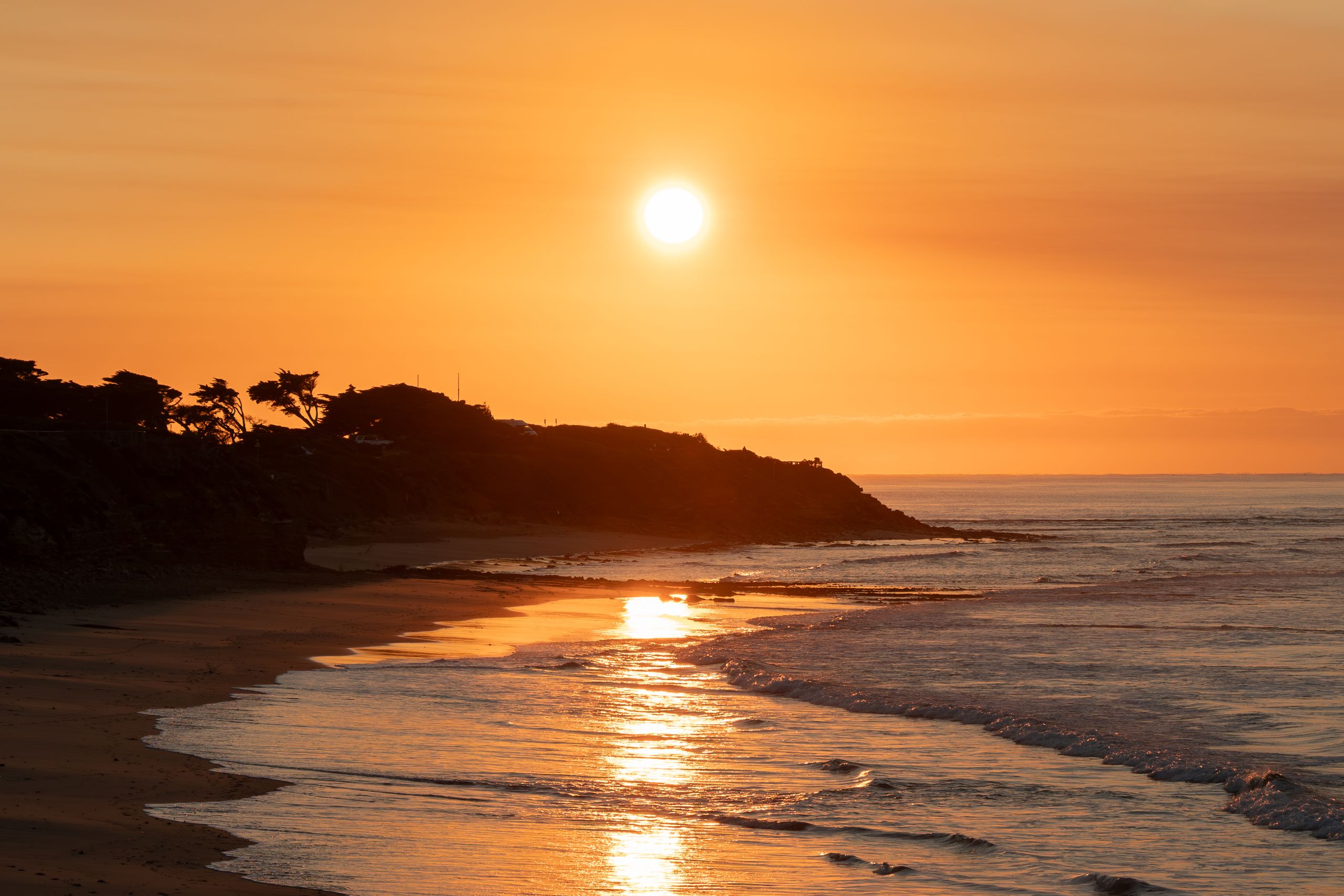 A stunning sunrise casts golden hues over Torquay Beach, Victoria, reflecting on the calm ocean waves.