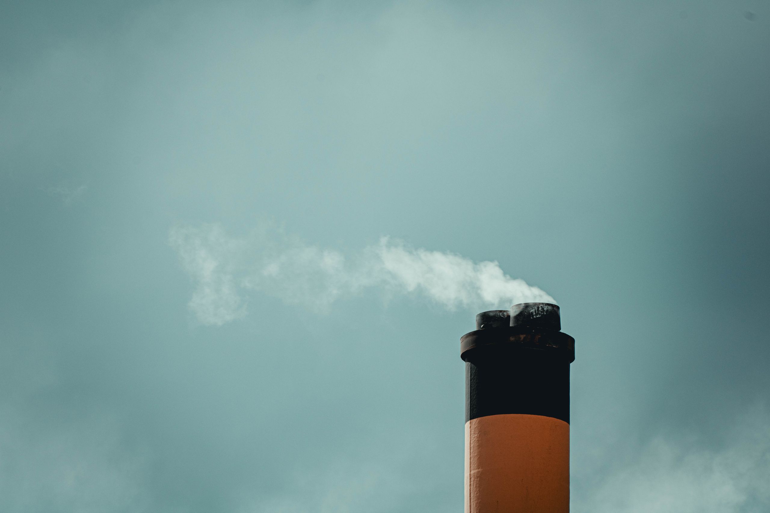 A tall chimney releasing smoke against a cloudy sky highlights industrial pollution.