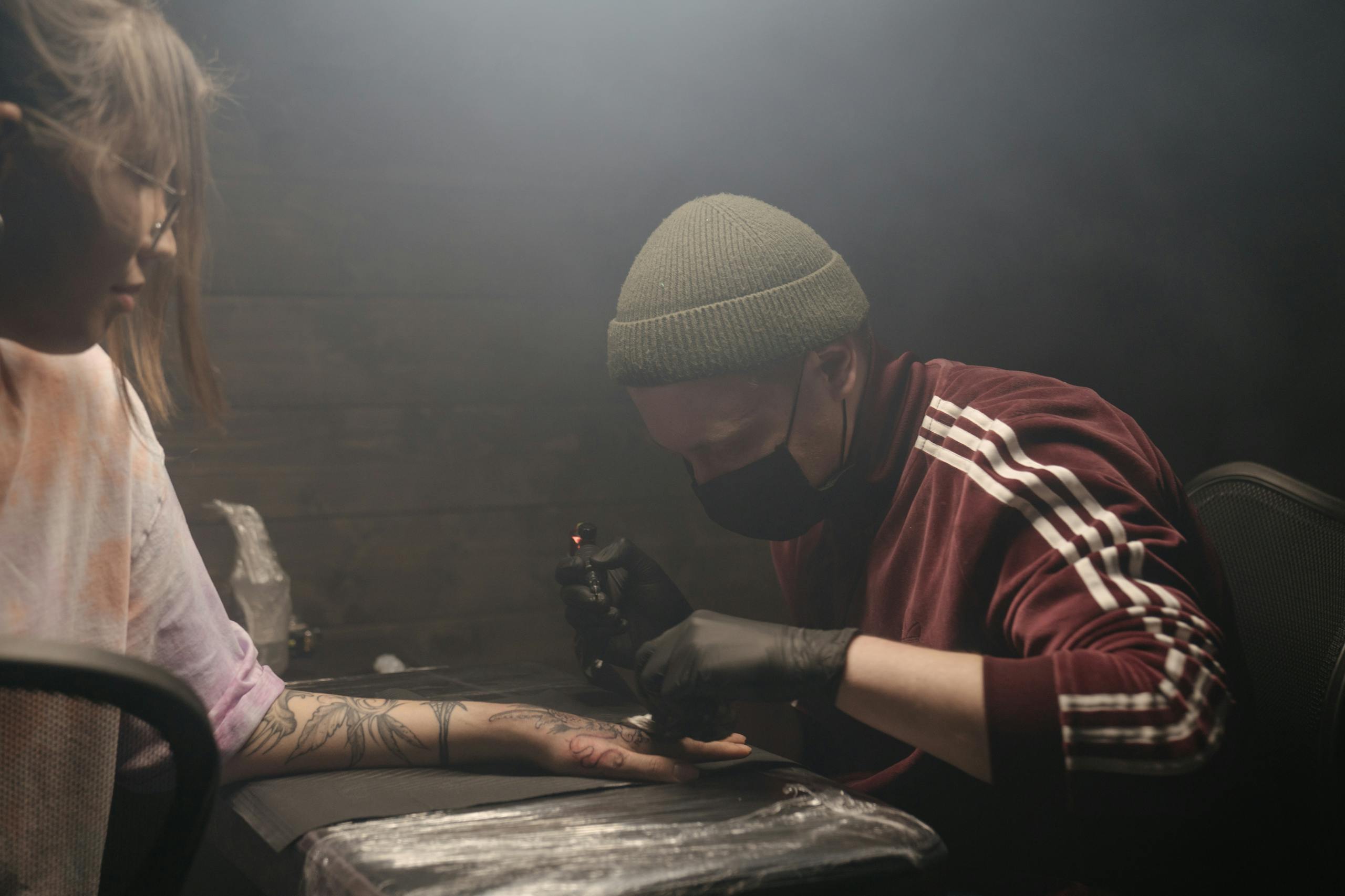 A tattoo artist inked in a studio, focusing on a detailed design on a client's arm.