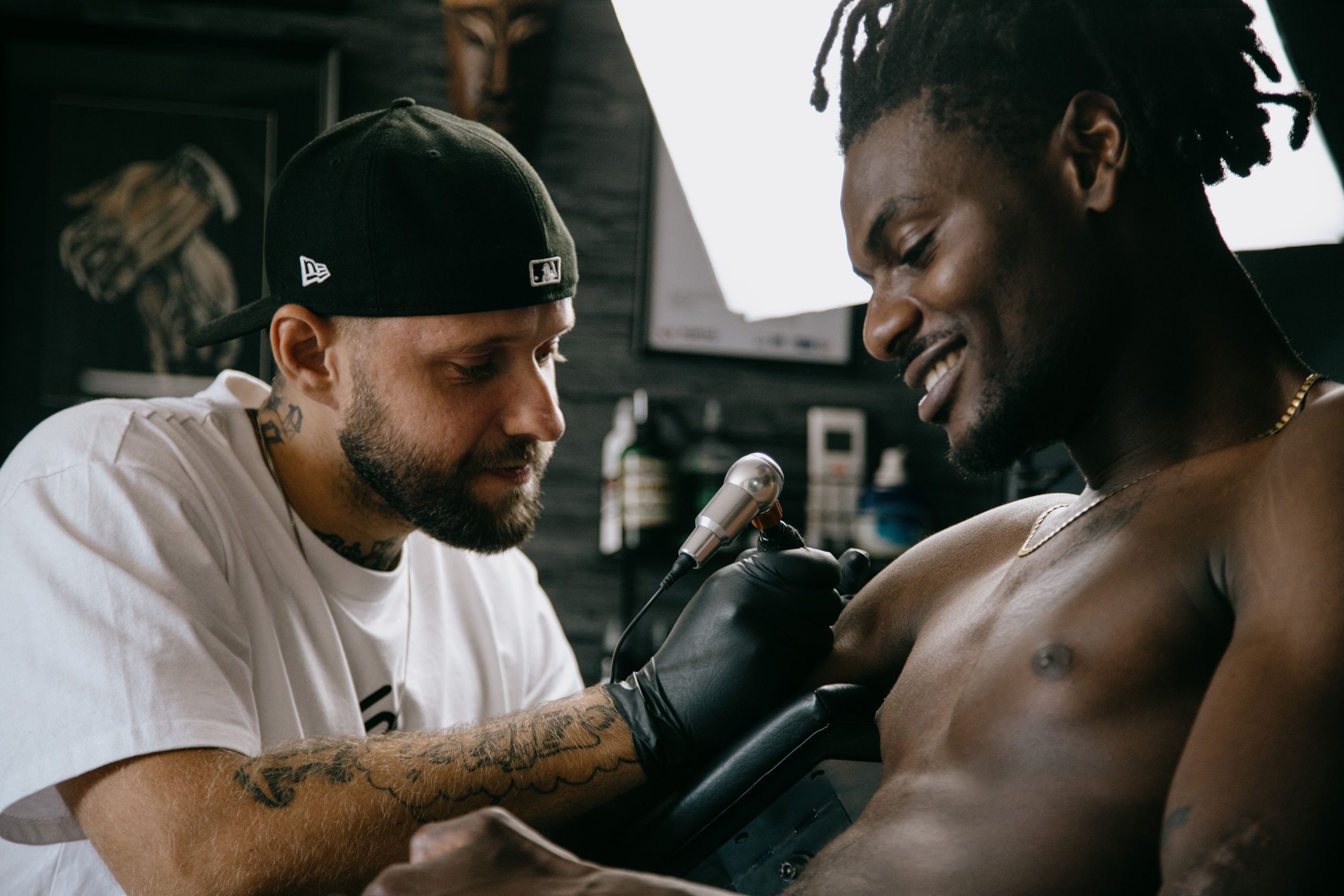 A tattoo artist inks a smiling topless client in a modern studio setting.
