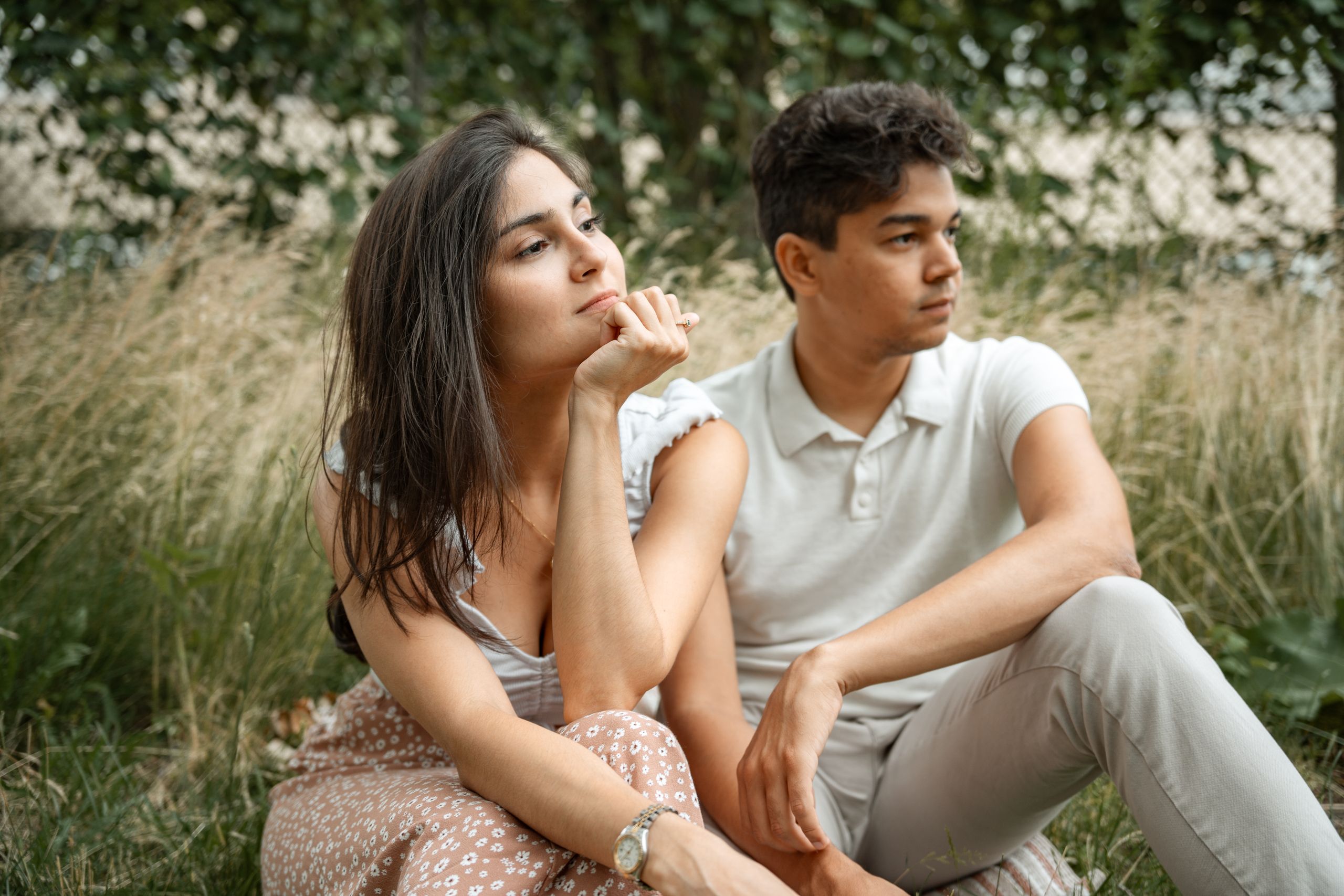 A thoughtful couple sitting together in a tranquil grassy field, enjoying the outdoors.