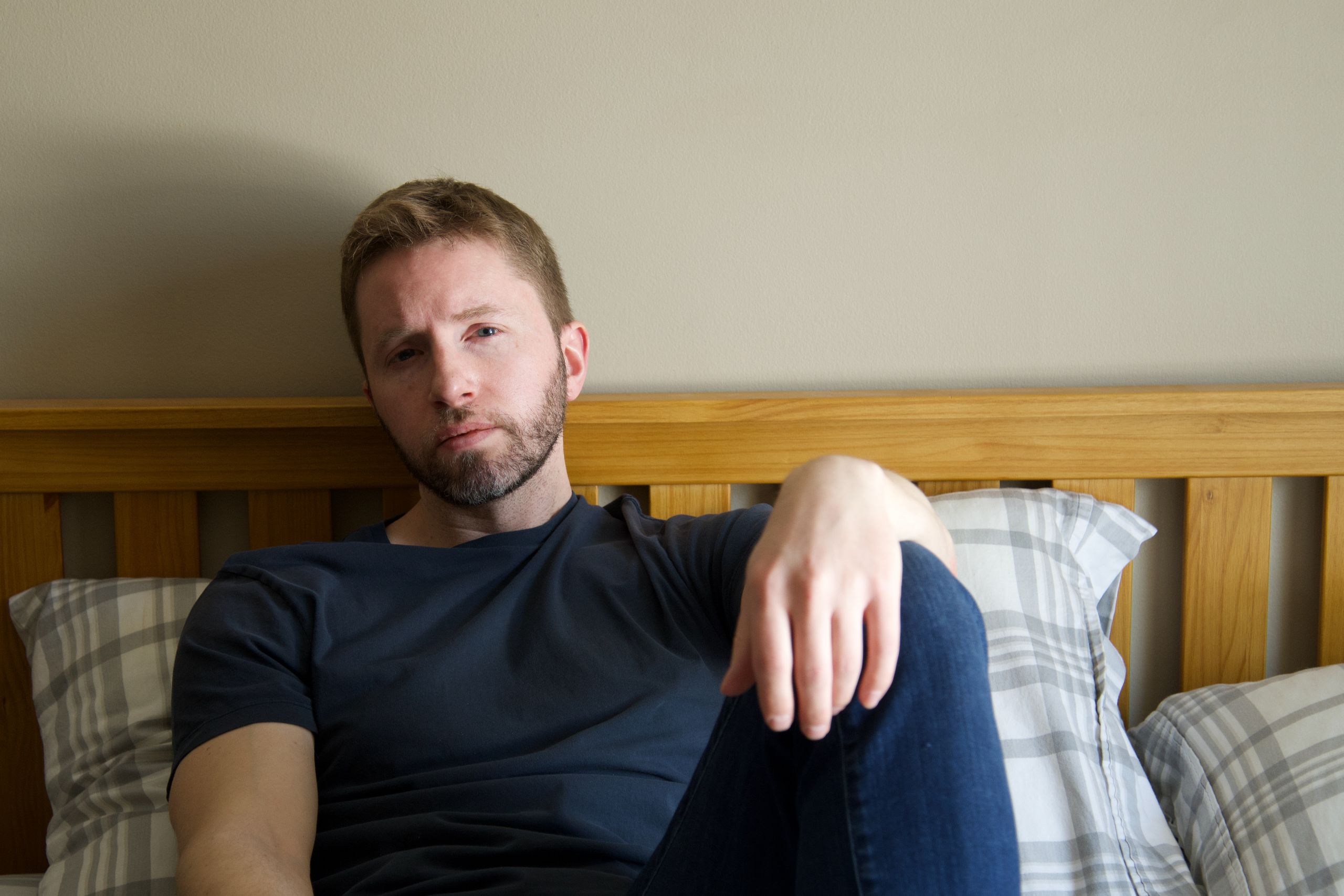A thoughtful man with a beard and mustache sits on a bed, exuding a sense of relaxation and introspection.