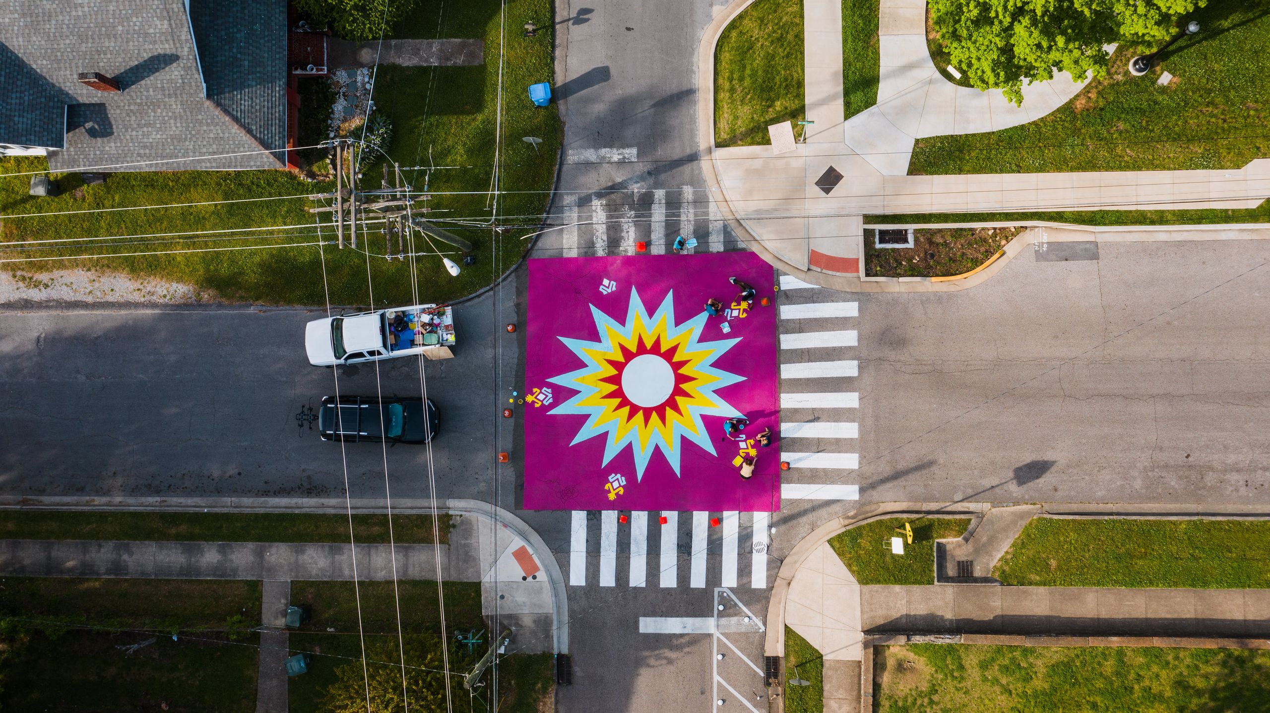 A vibrant aerial shot of a street intersection with a bold geometric artwork at the center.