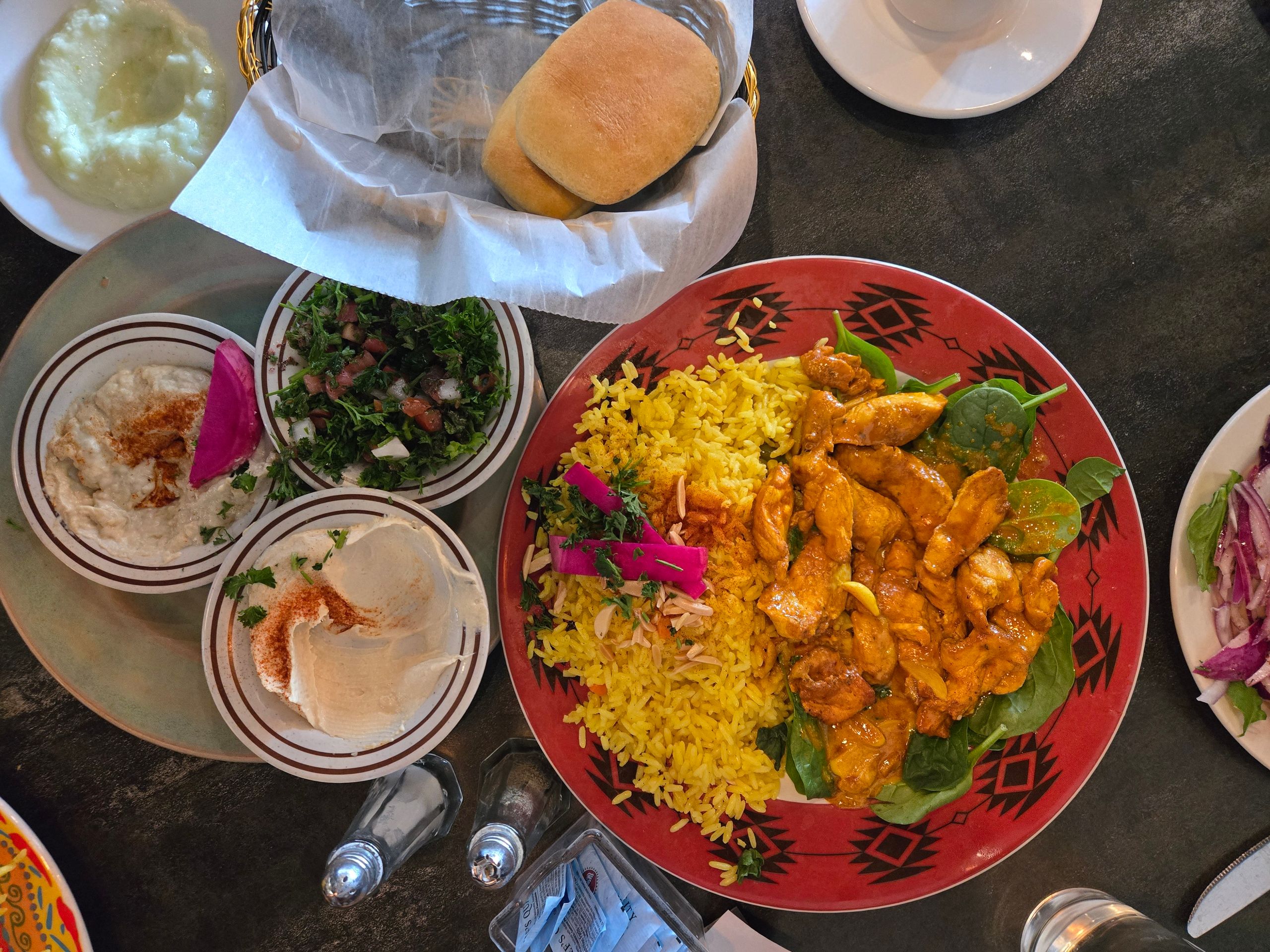 A vibrant Middle Eastern meal featuring chicken curry, rice, hummus, salad, and bread.
