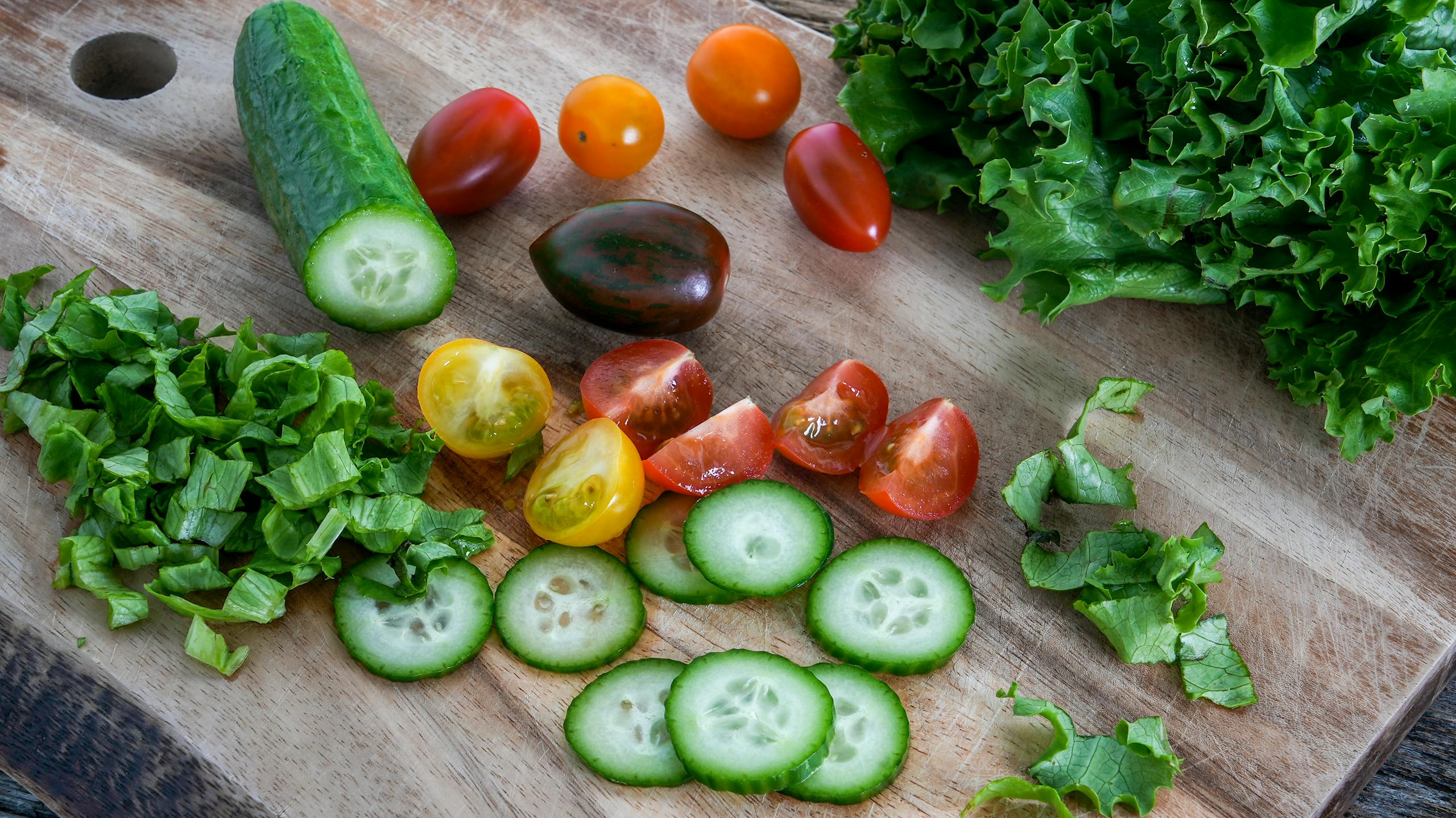 A vibrant mix of sliced cucumbers, cherry tomatoes, and lettuce on a wooden cutting board, perfect for salads.