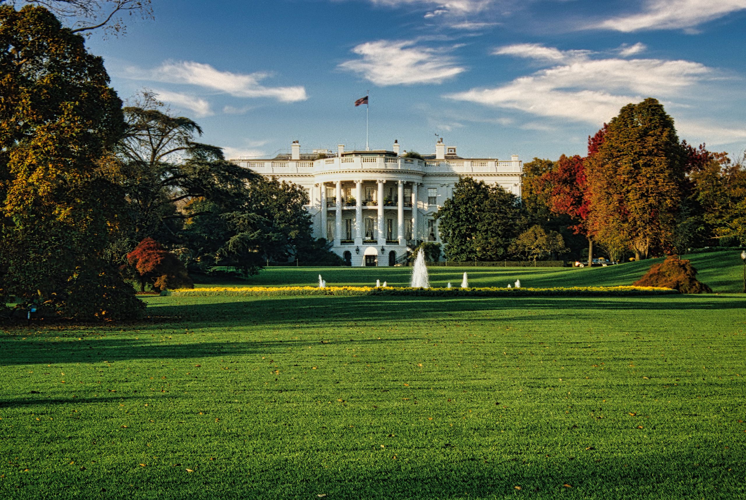 A view of the White House surrounded by autumn foliage and a central fountain in Washington, DC.