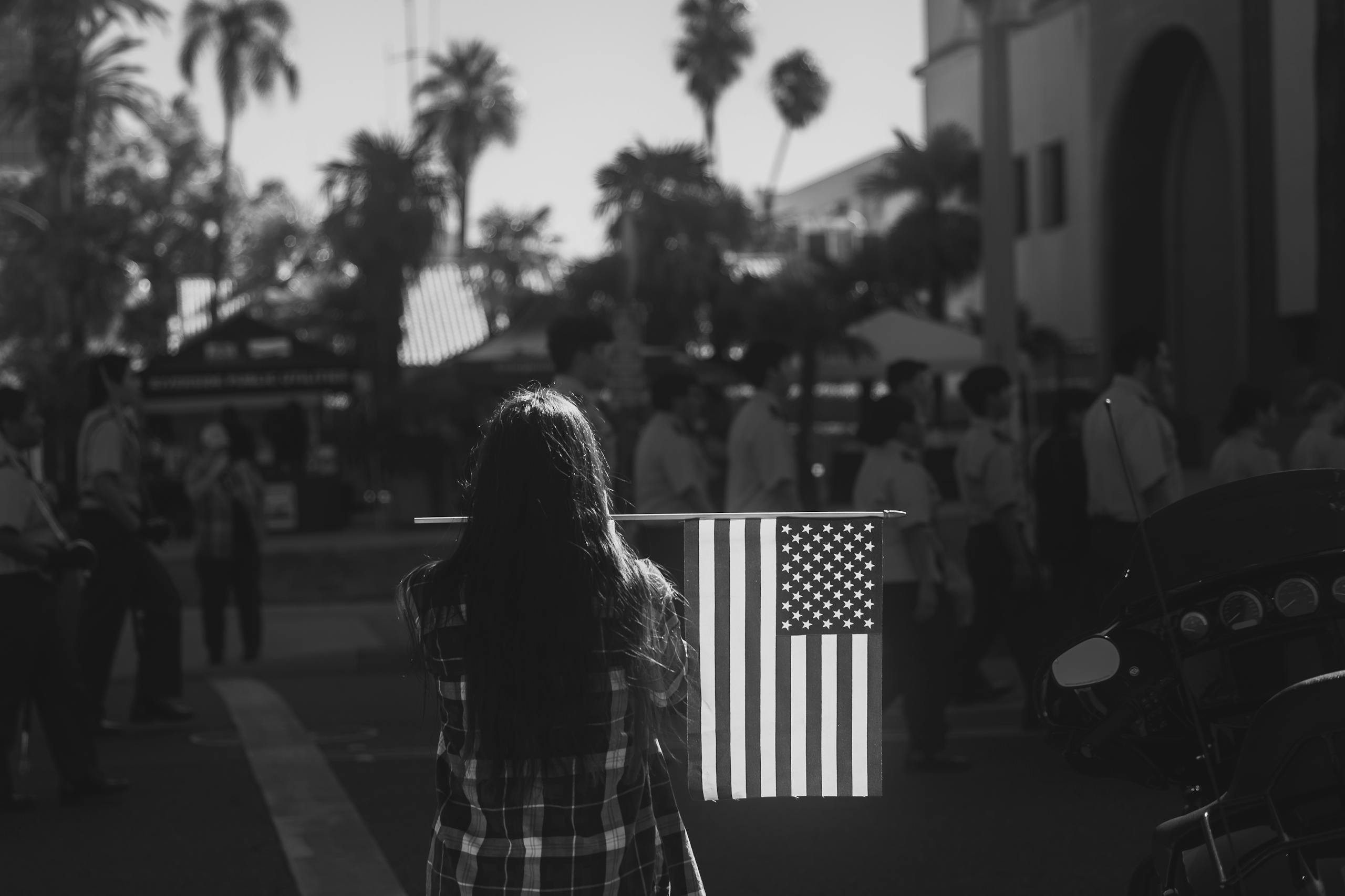 A woman holding an American flag at a parade event in a city setting, symbolizing patriotism.