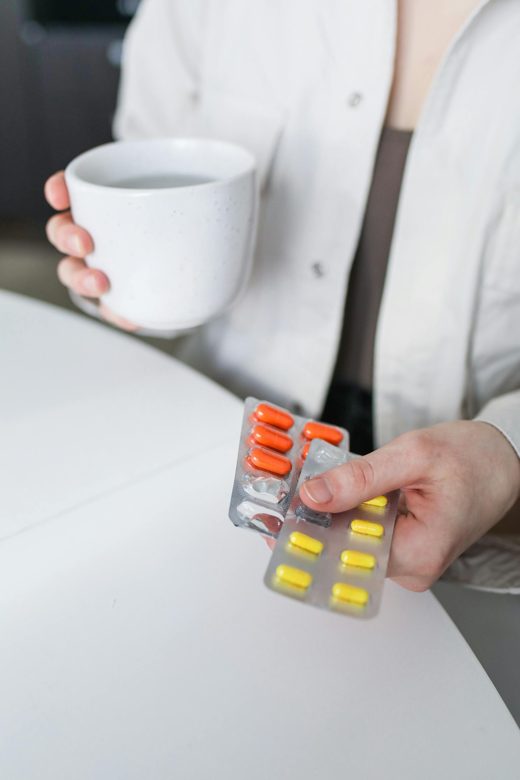 A woman holding blister packs of pills and a mug of tea, symbolizing treatment for illness.