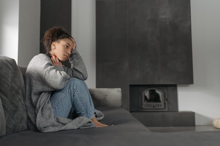 A woman in a cozy living room feeling unwell, sitting on a sofa with a thoughtful expression.