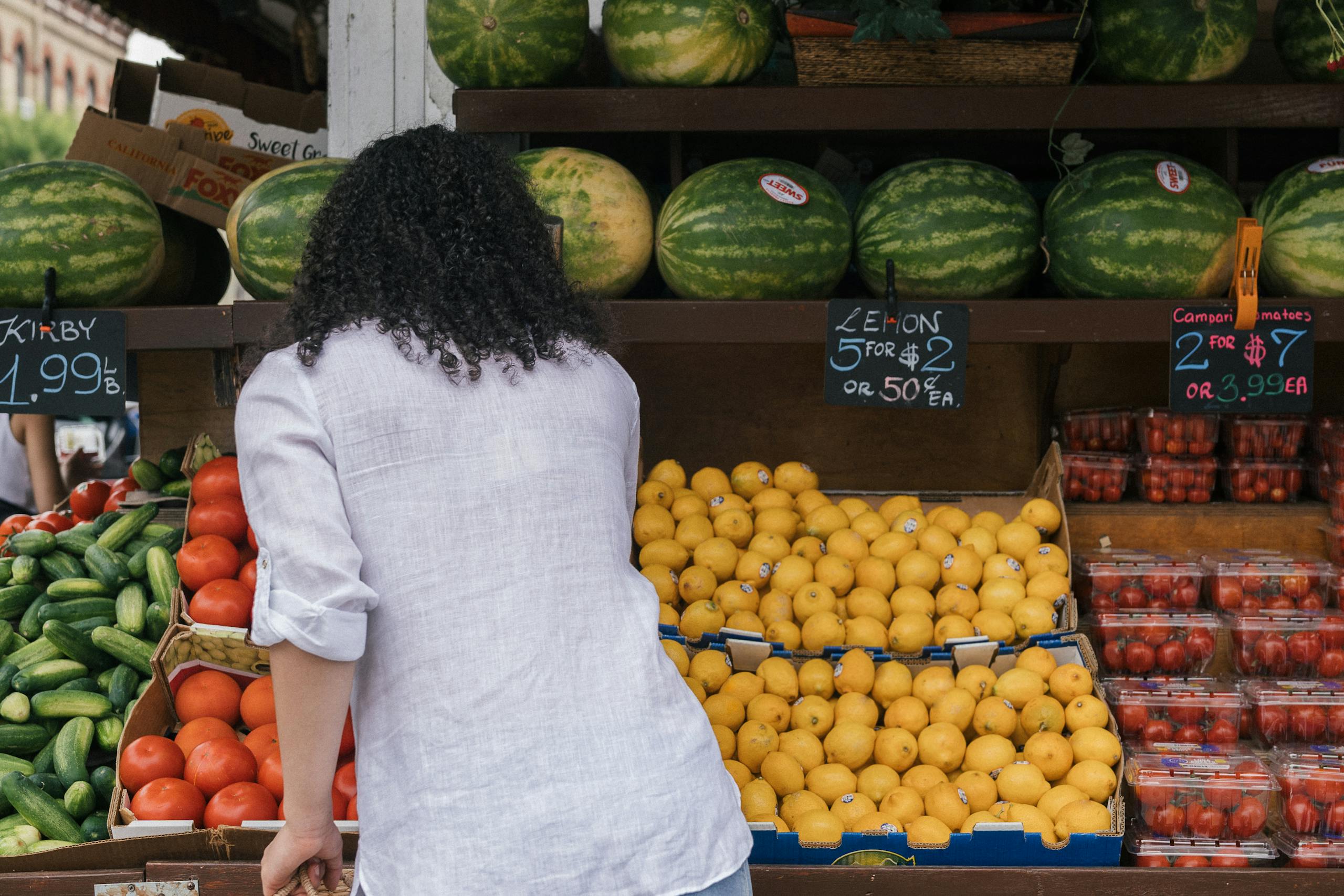 A woman selects produce at an outdoor fruit market with diverse fresh fruits.